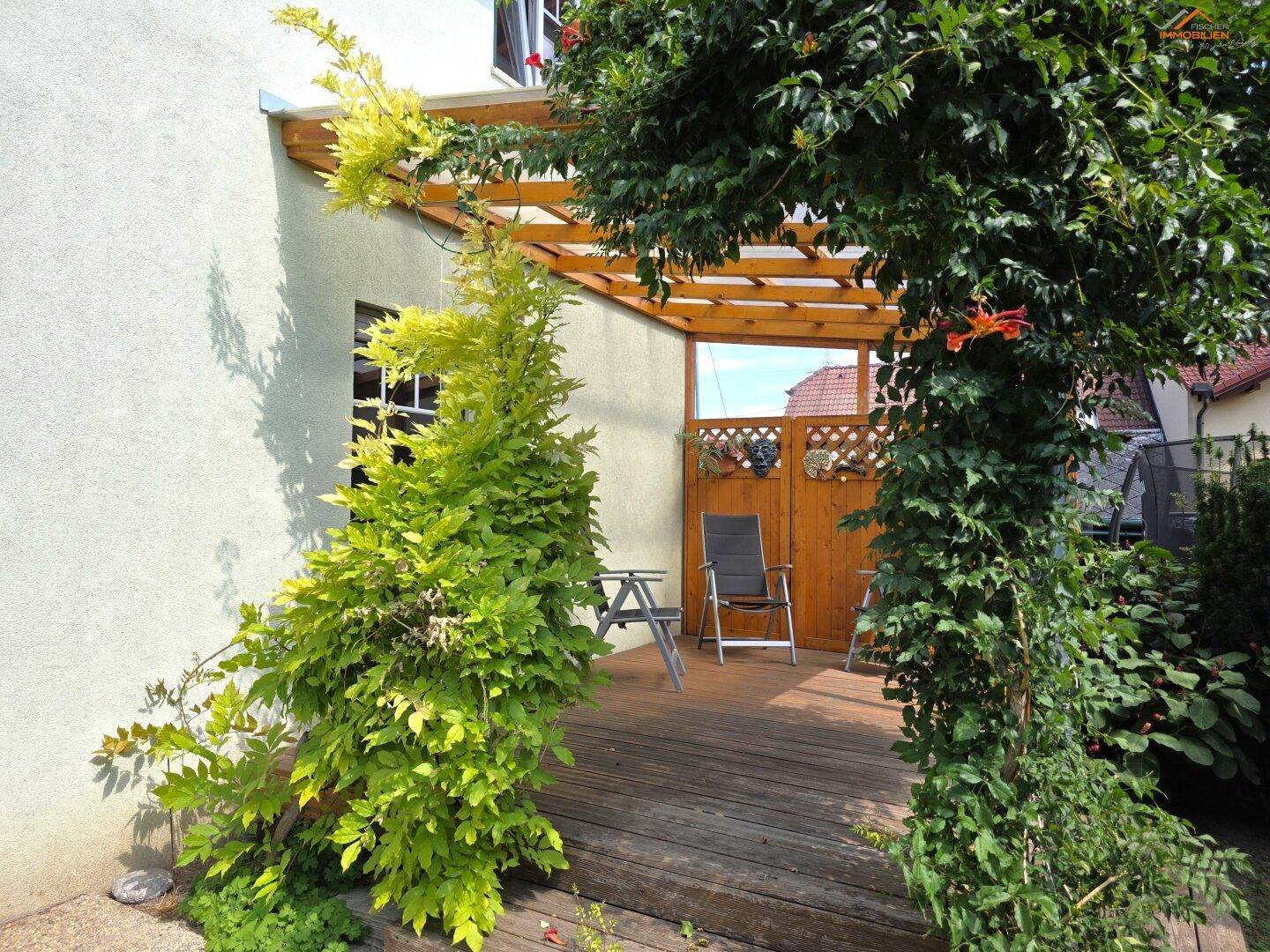 Gemütliche überdachte Holzterrasse mit Sitzgelegenheiten und üppiger Bepflanzung.