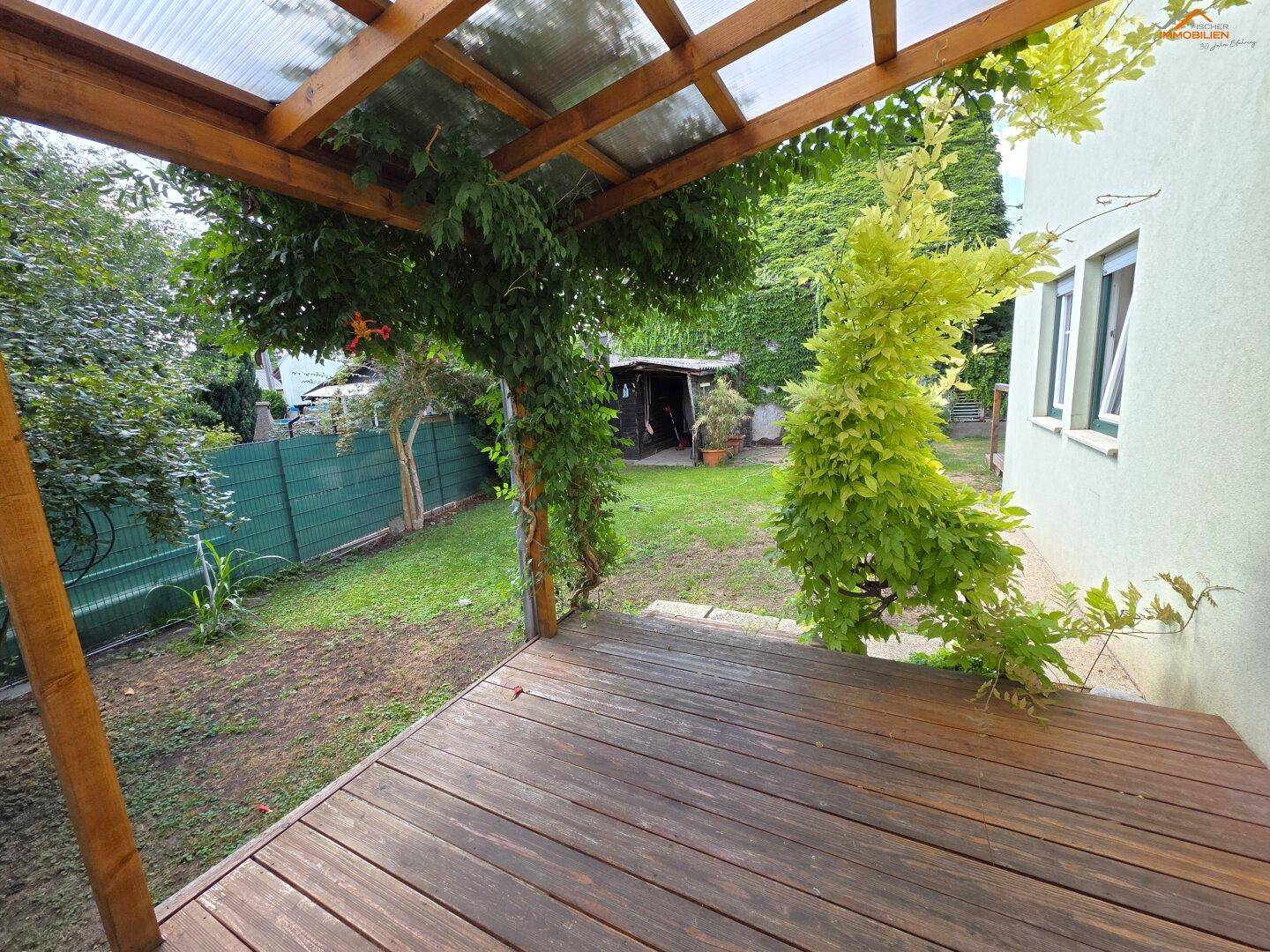 Überdachte Holzterrasse mit Kletterpflanzen und Blick auf den Gartenbereich.