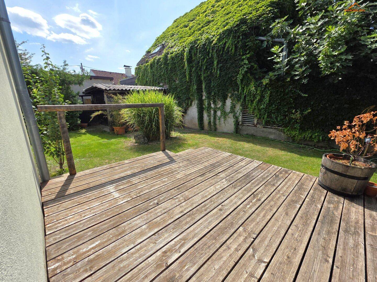 Holzterrasse mit Blick auf den grünen Garten und das von Efeu bewachsene Haus.