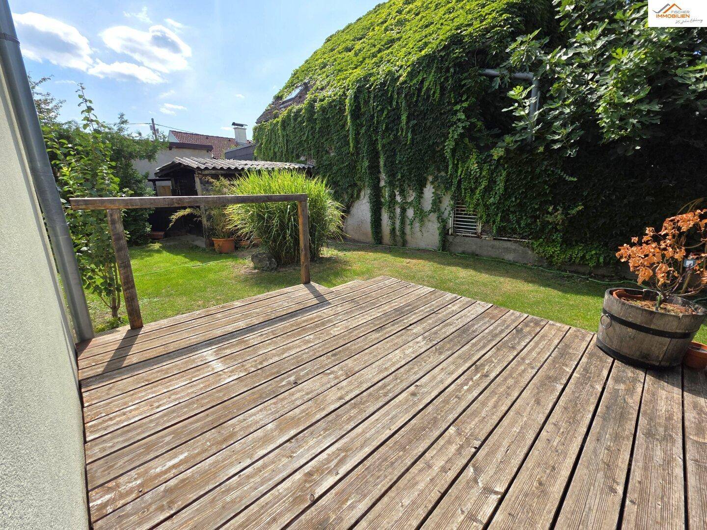Holzterrasse im Garten mit Blick auf das von Efeu bewachsene Haus und den grünen Rasen.