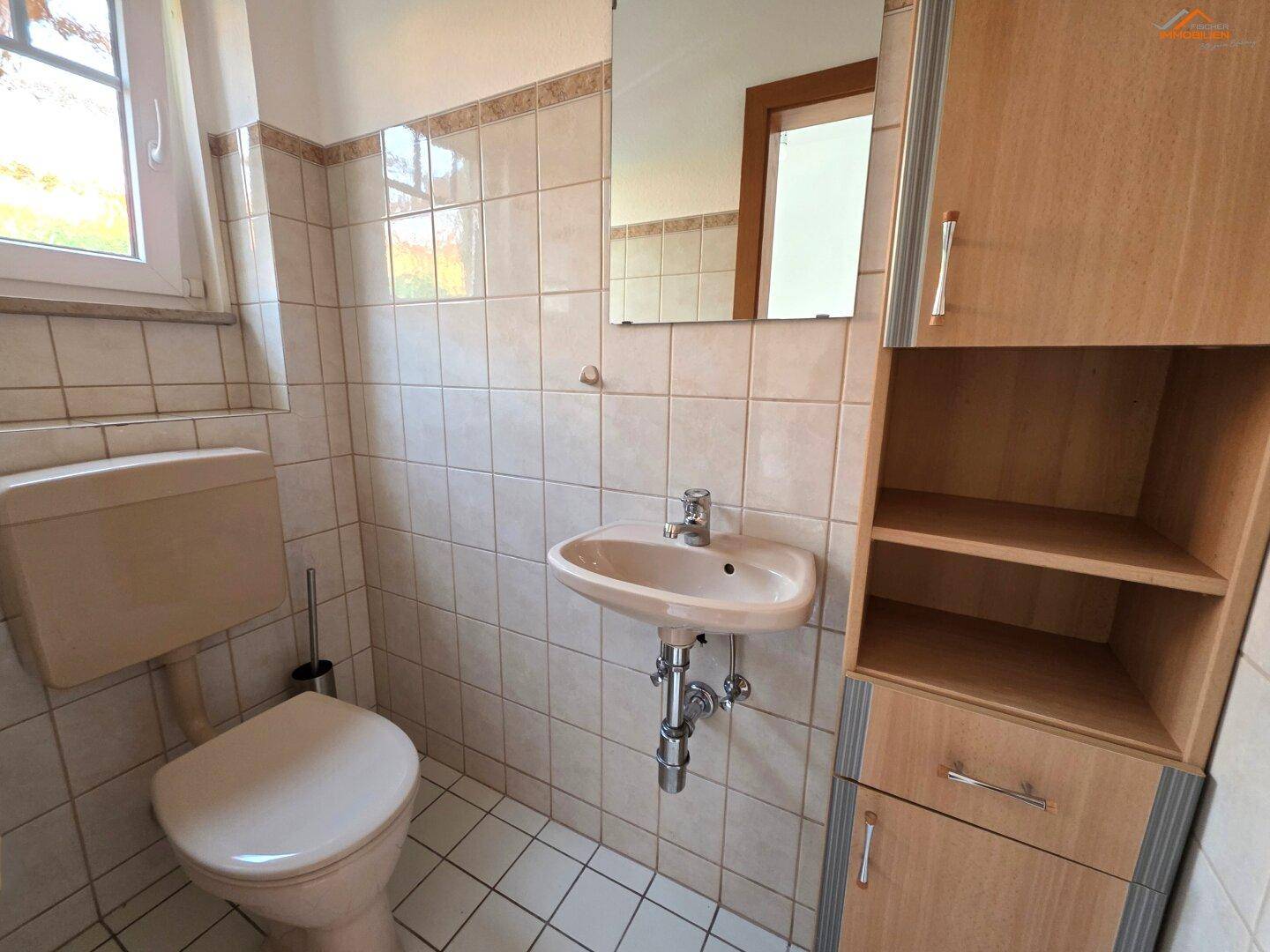 Kleines Gäste-WC mit beigen Fliesen, Waschbecken und WC, sowie einem Fenster.