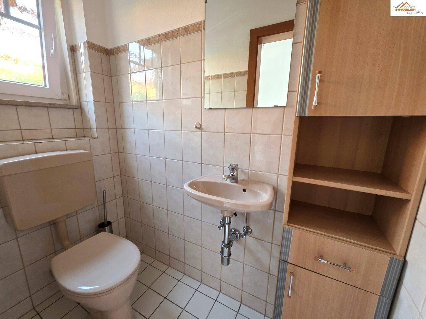 Kleines Badezimmer mit beigefarbenen Fliesen, WC, Waschbecken und einem Spiegelschrank.