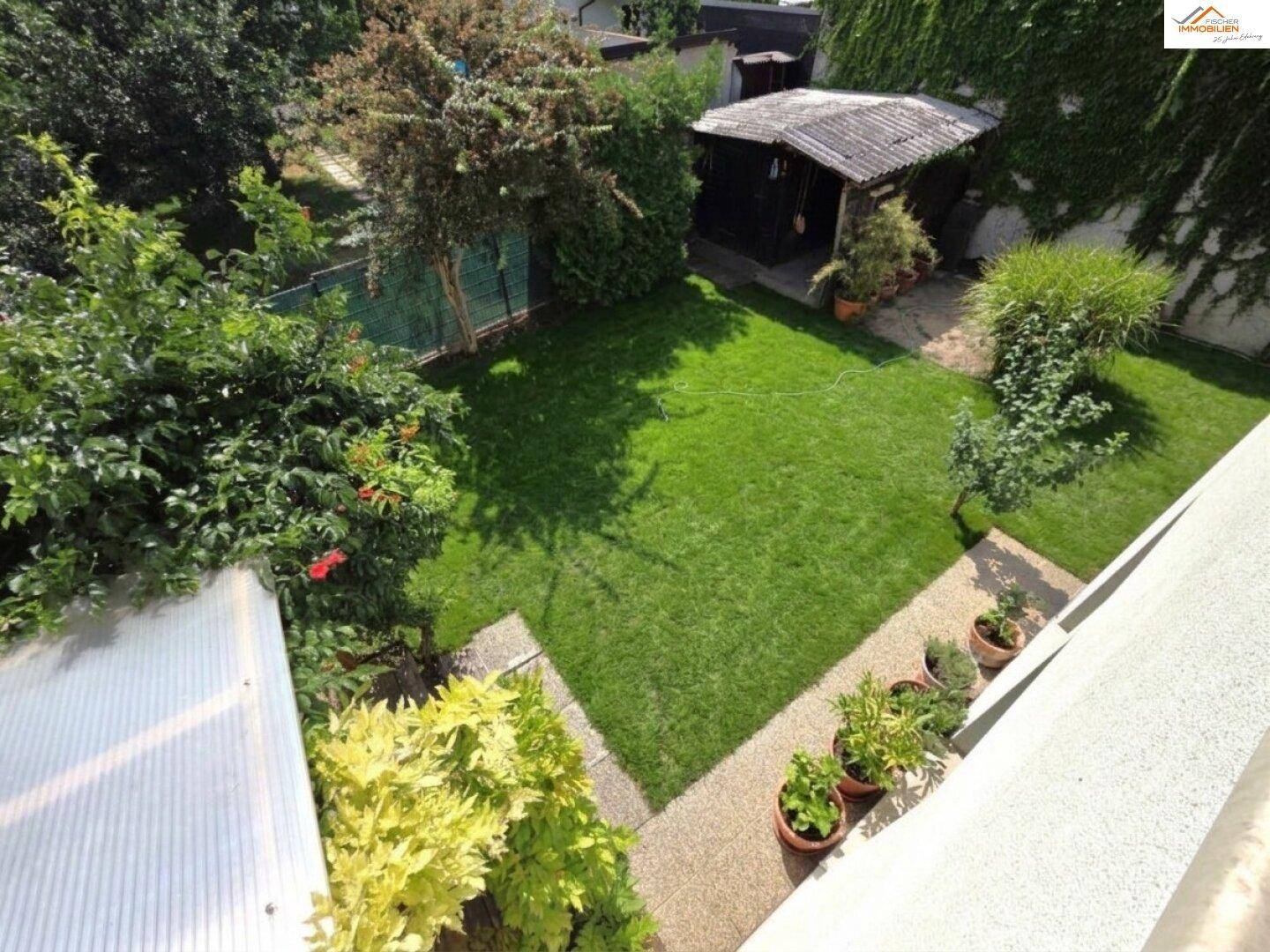 Vogelperspektive des Gartens mit Rasenfläche, gepflastertem Weg und verschiedenen Pflanzen.