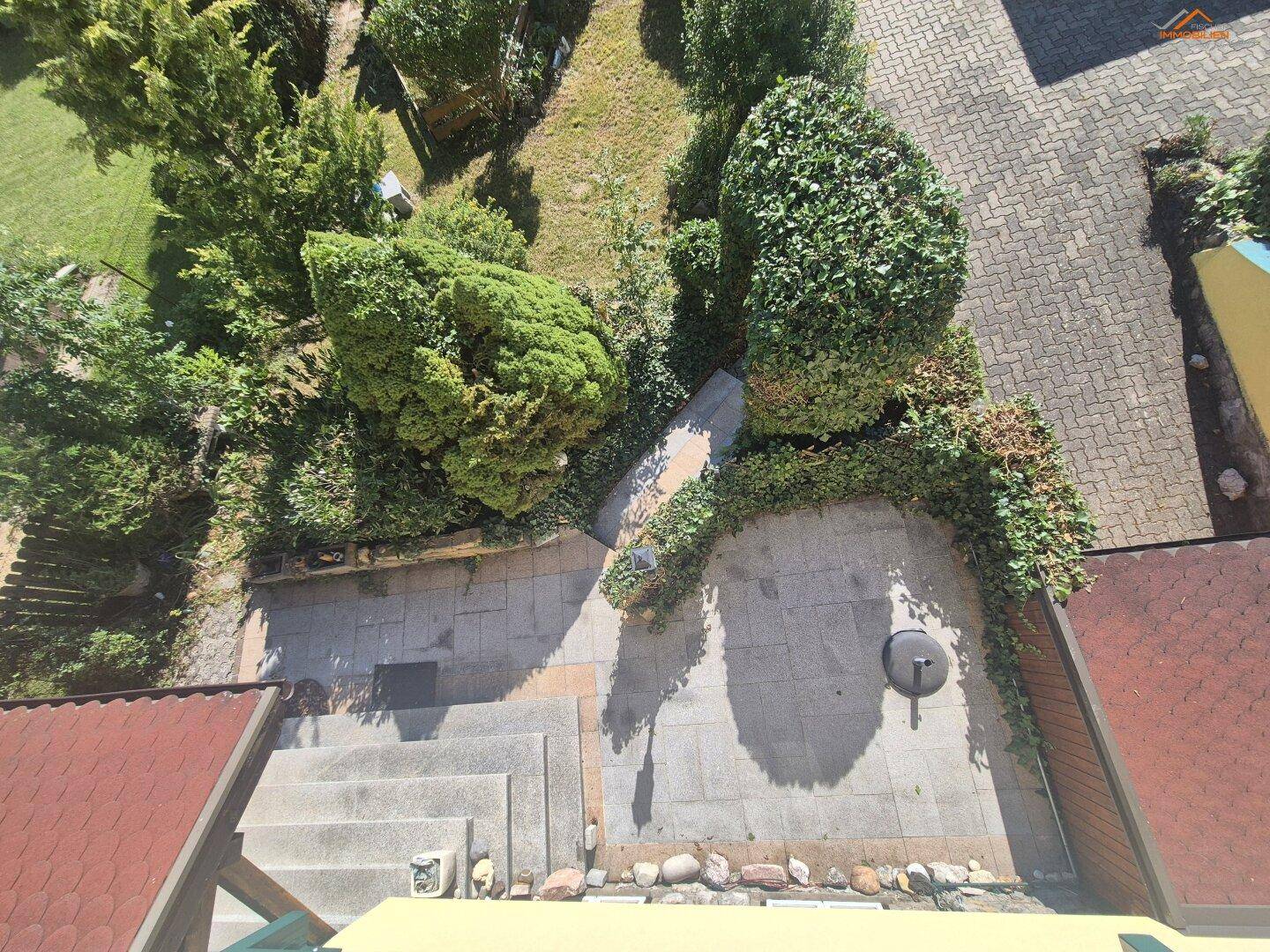 Blick von oben auf einen gepflasterten Terrassenbereich mit Steinstufen und angrenzendem Garten.