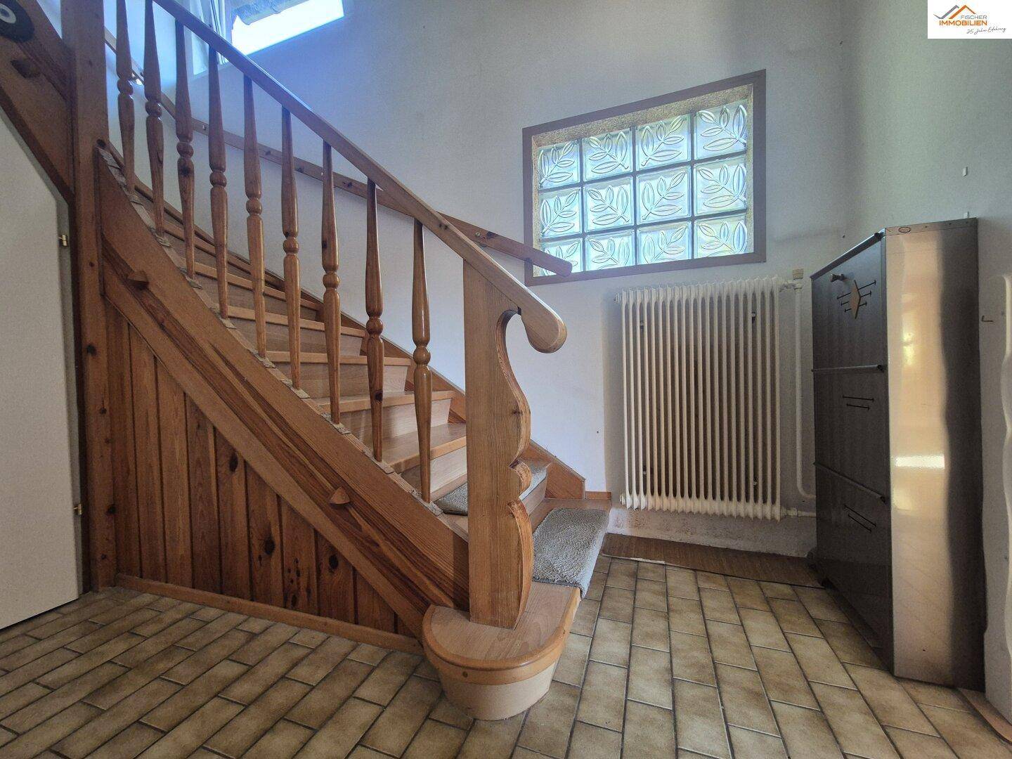 Hölzerne Treppe im Flur mit Fliesenboden, Heizkörper und einem Fenster aus Glasbausteinen.