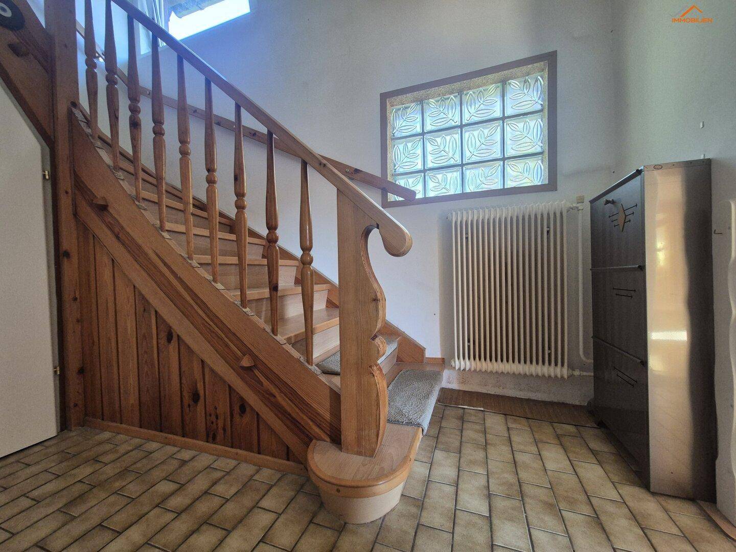Flur mit rustikaler Holztreppe, Fliesenboden und einem dekorativen Fenster aus Glasbausteinen.