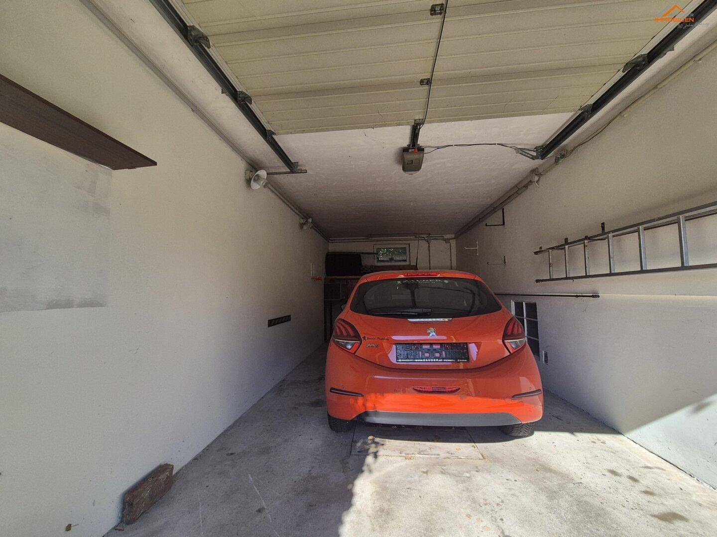 Geräumige Garage mit einem geparkten Auto und praktischem Stauraum an den Wänden.
