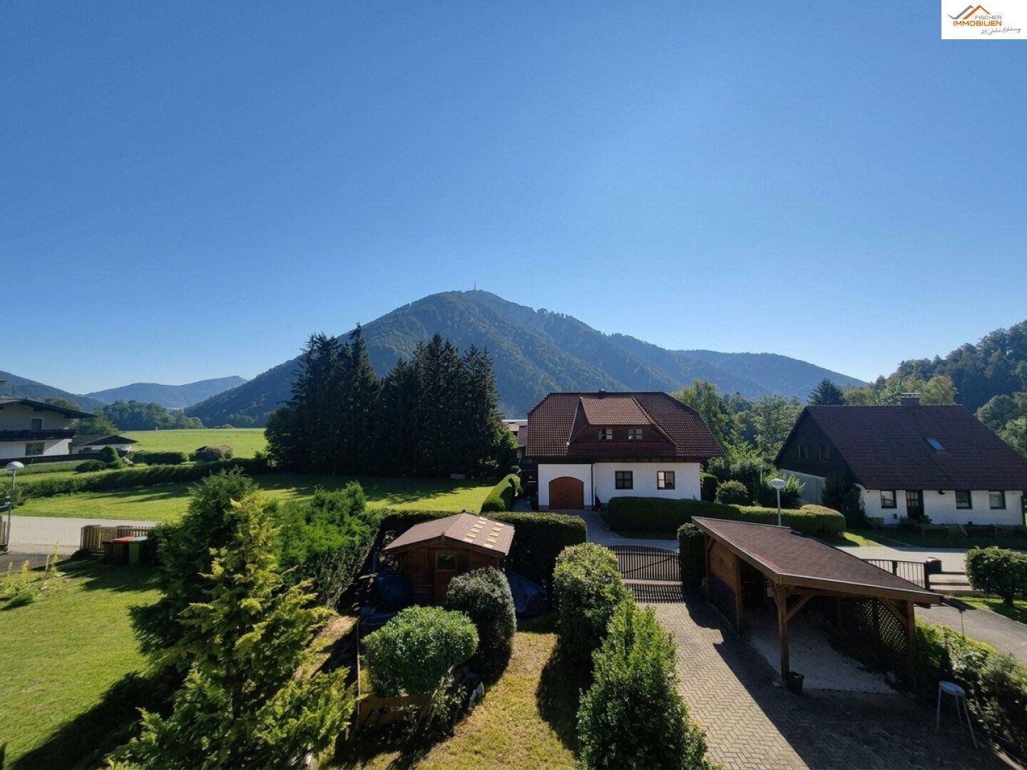 Weitläufiger Blick auf die ländliche Umgebung mit Häusern, grünen Wiesen und Bergen im Hintergrund.