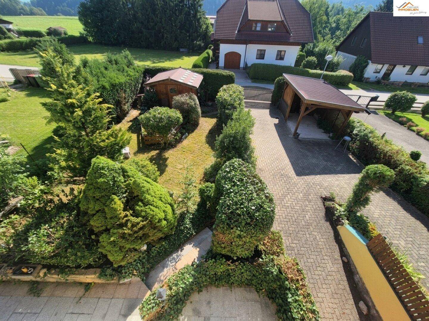 Vogelperspektive auf den gepflegten Gartenbereich mit Carport, Schuppen und viel Grün.