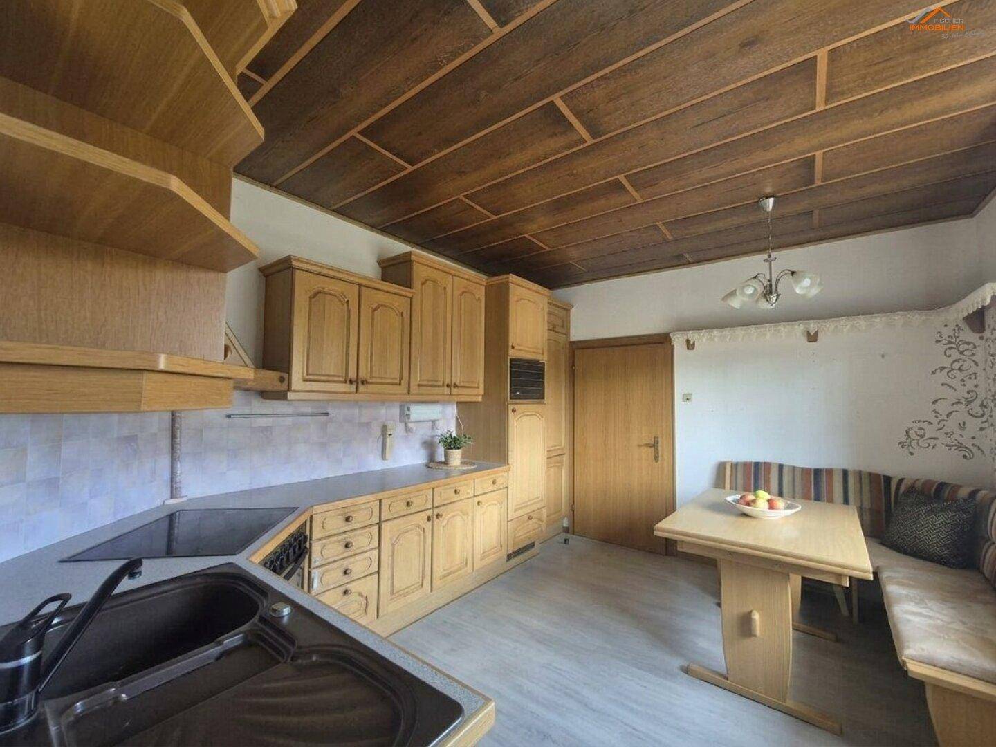 Traditionelle Holzküche mit Essbereich, Einbauschränken und charakteristischer Holzdeckenverkleidung.