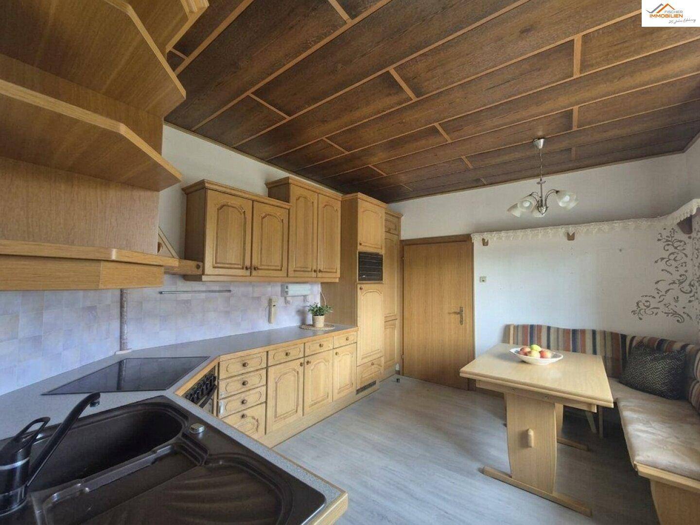 Rustikale Küche mit Holzeinbauten, Essbereich und charakteristischer Holzdeckenverkleidung.