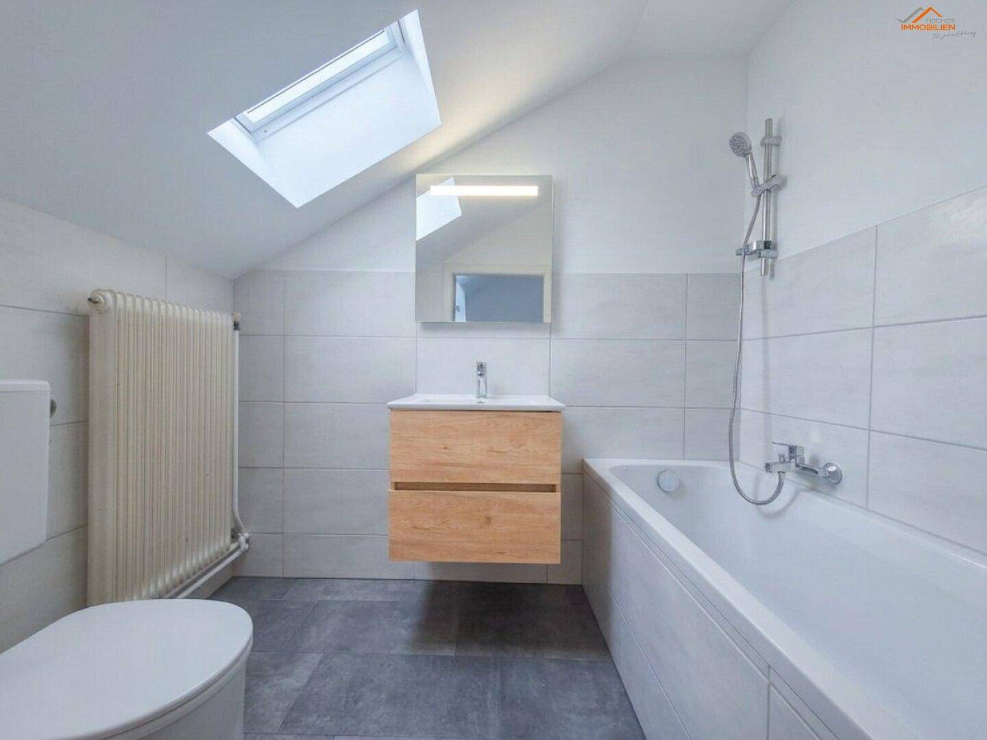 Modernisiertes Badezimmer mit Dachfenster, Badewanne, schwebendem Waschtisch und hellen Fliesen.