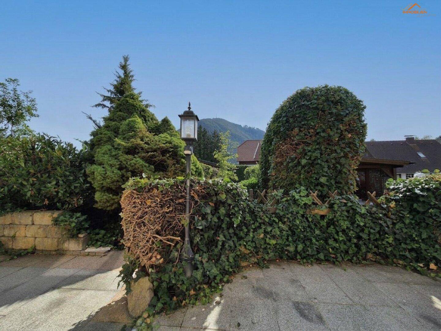 Gartenbereich mit einer dekorativen Laterne, dichten Hecken und Blick auf die umliegende Landschaft.