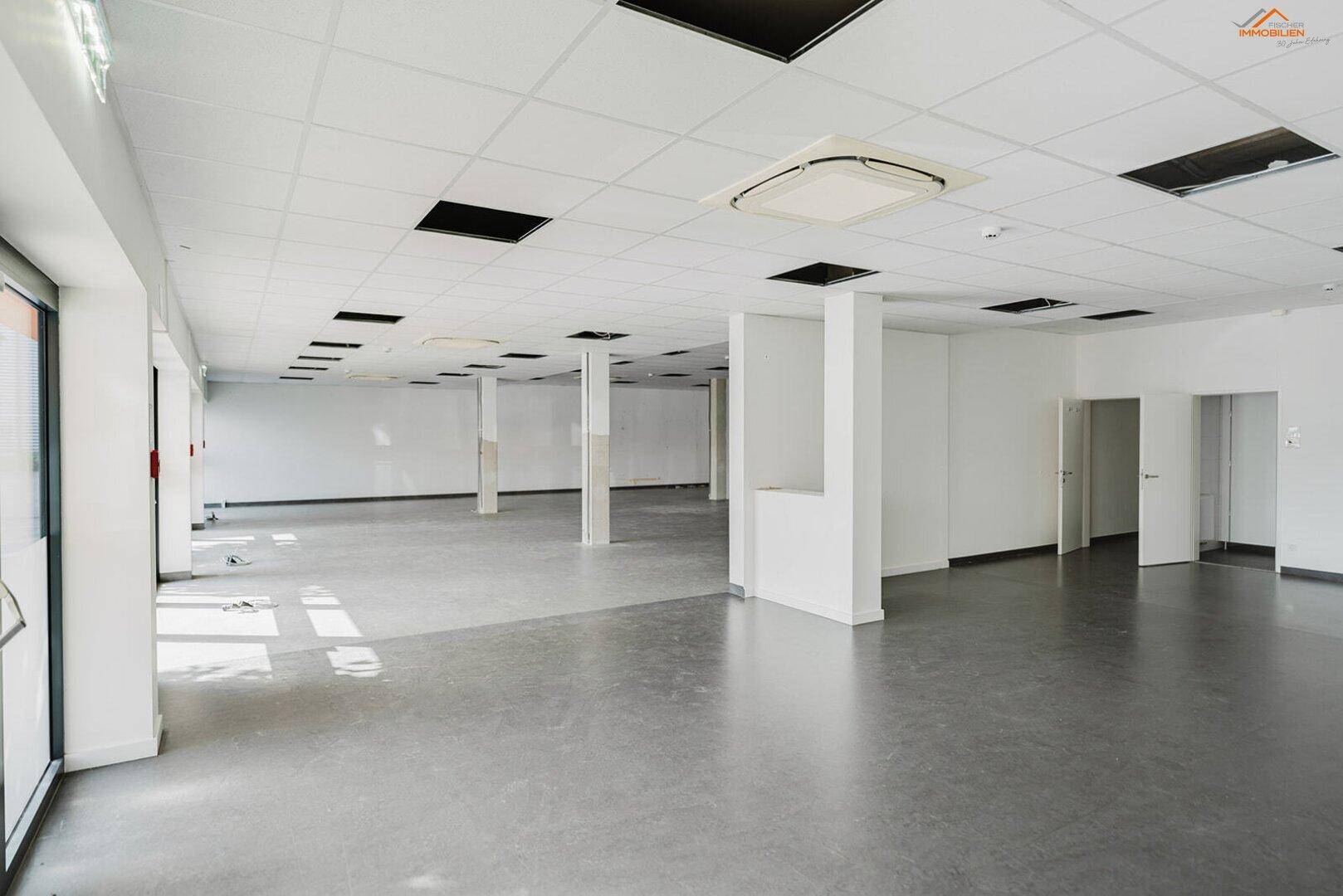 Weitläufiger, leerer Gewerberaum mit Säulen, abgehängter Decke und schlichten weißen Wänden, bereit zur Gestaltung.