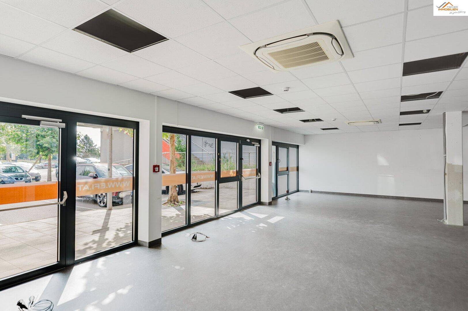 Heller Gewerberaum mit großen Glasfronten, die viel Tageslicht hereinlassen, und abgehängter Decke.
