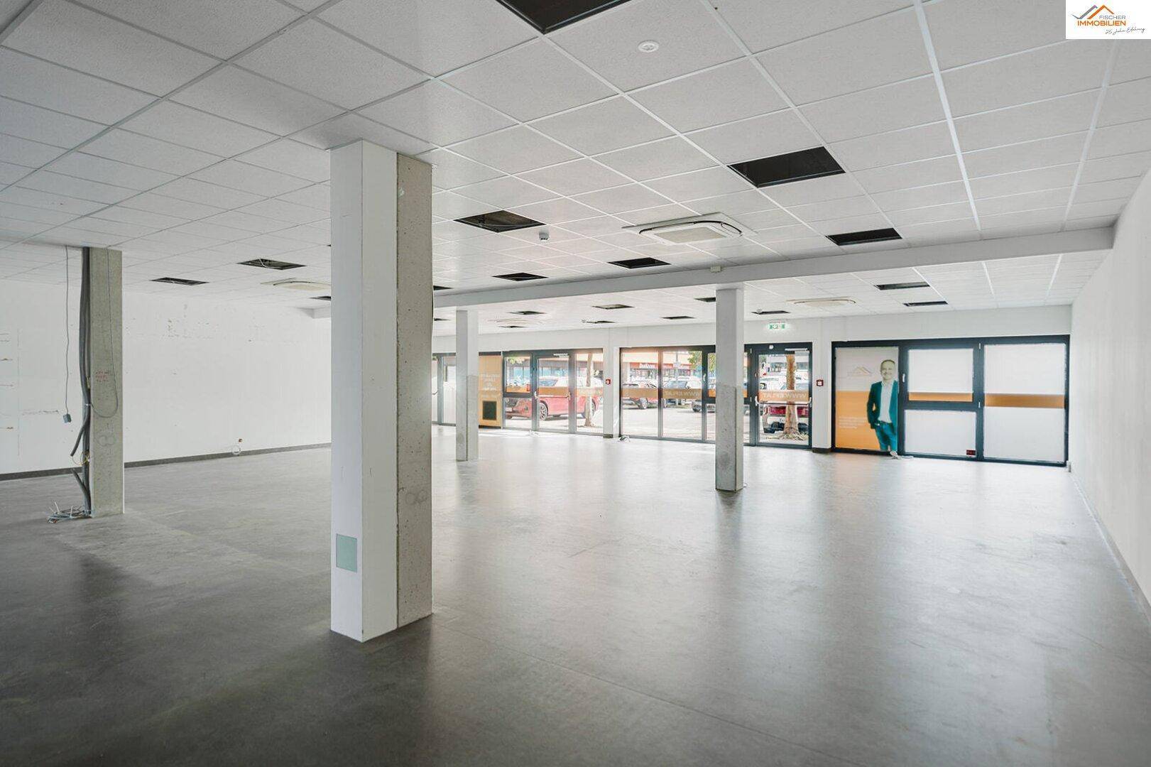 Heller Gewerberaum mit großen Fensterfronten, Säulen und einem modernen abgehängten Deckensystem.