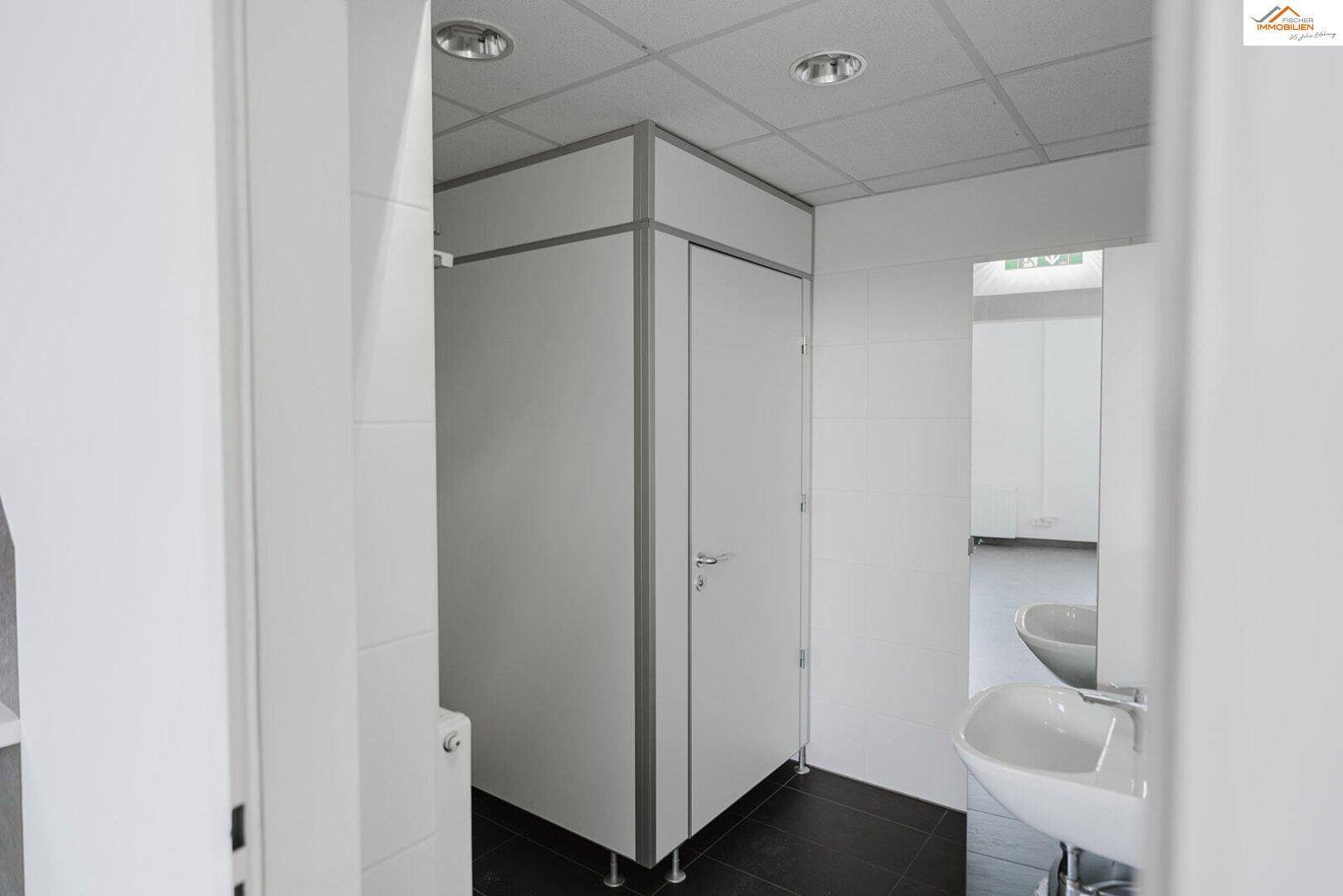 Moderne Toilettenkabinen mit dunklen Fliesen und weißen Waschbecken in einem gepflegten Sanitärbereich.