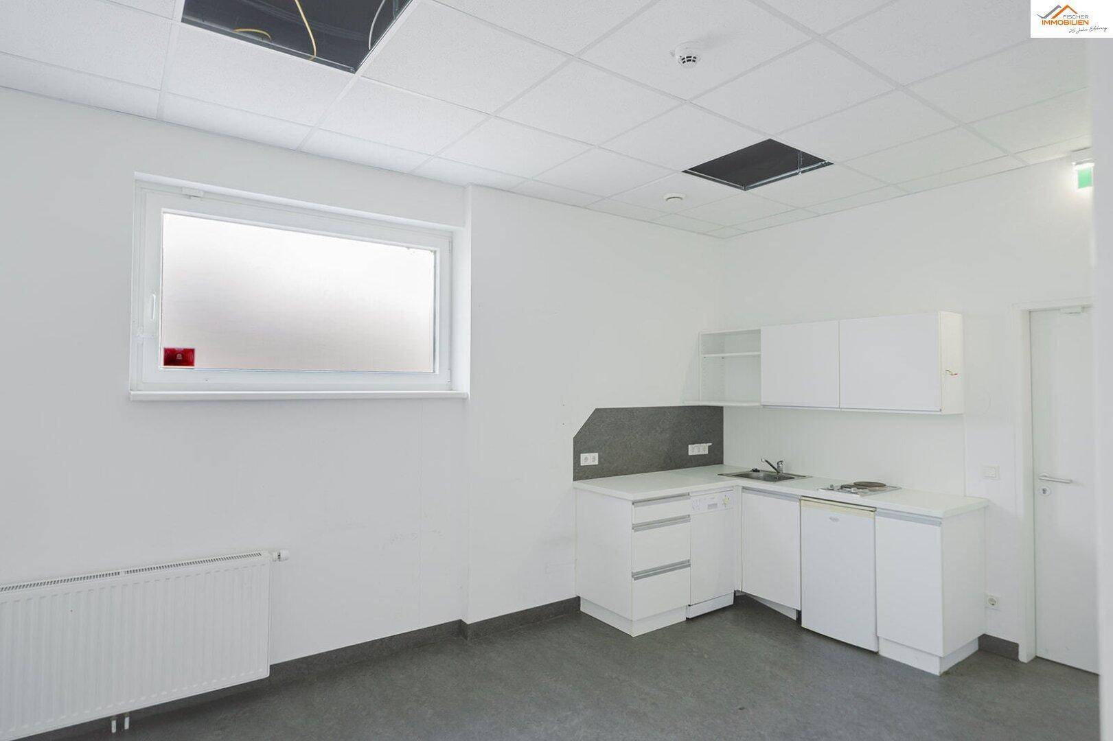 Kleine Einbauküche mit weißen Schränken, Spüle und Fenster in einem hellen Raum.