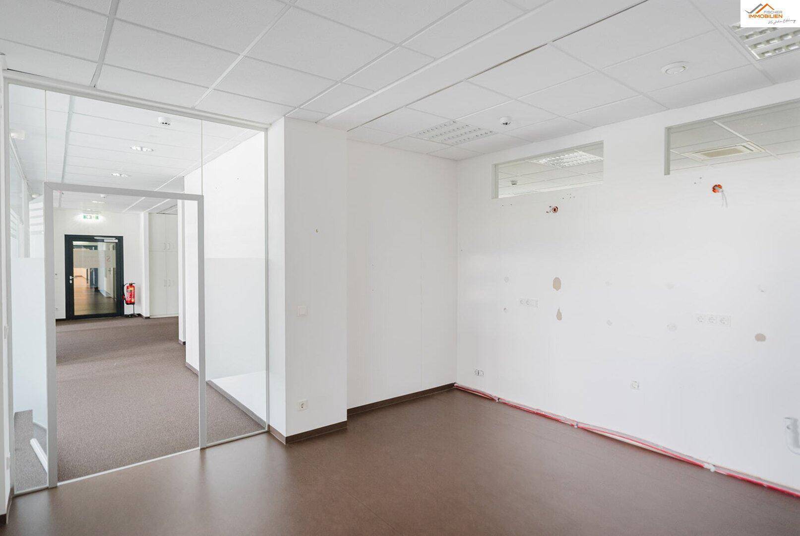 Büroflur mit Teppichboden, Glaswänden und Blick in einen weiteren Bürobereich.