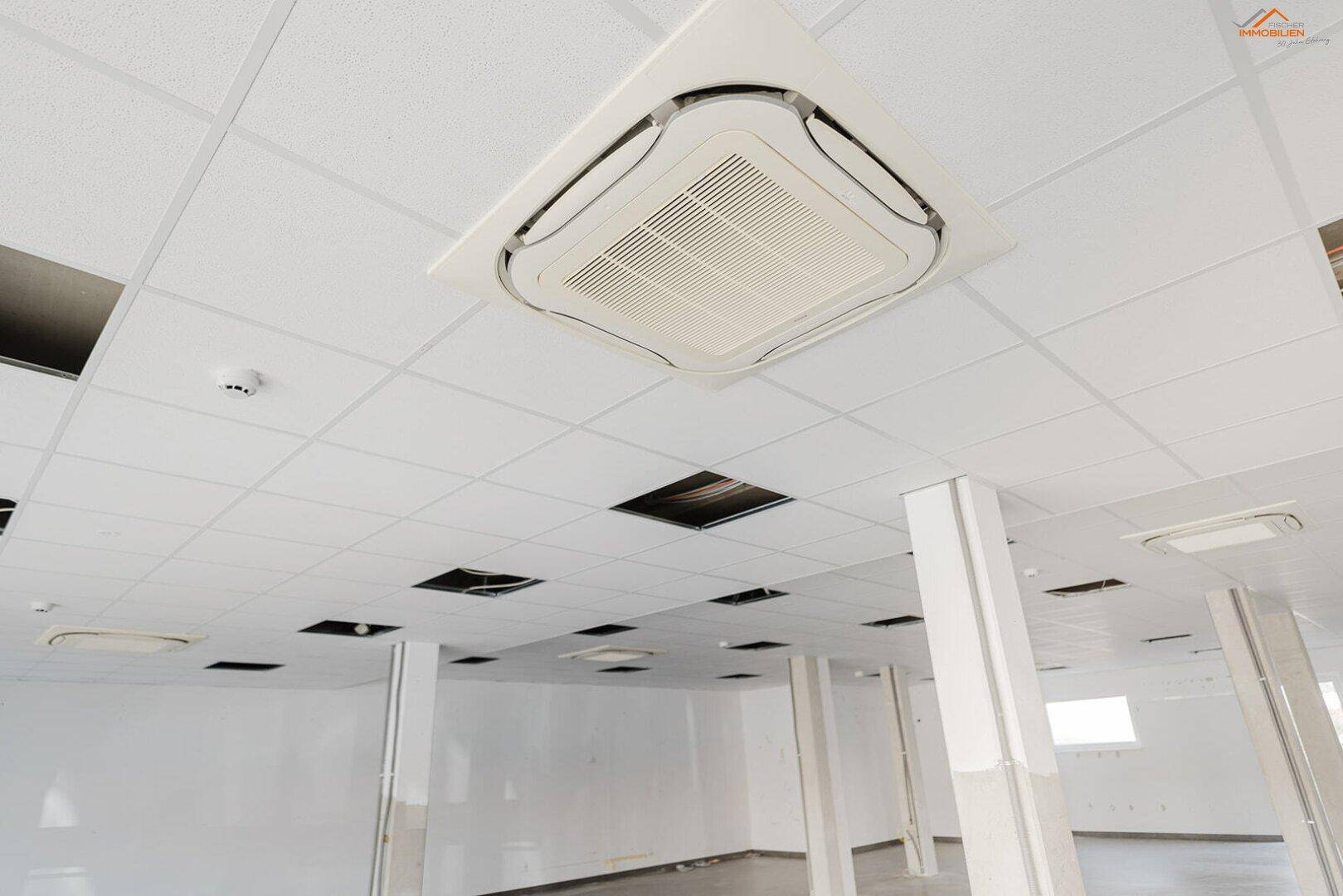 Deckenmontierte Klimaanlage in einem Gewerberaum mit Rasterdecke und integrierter Beleuchtung.