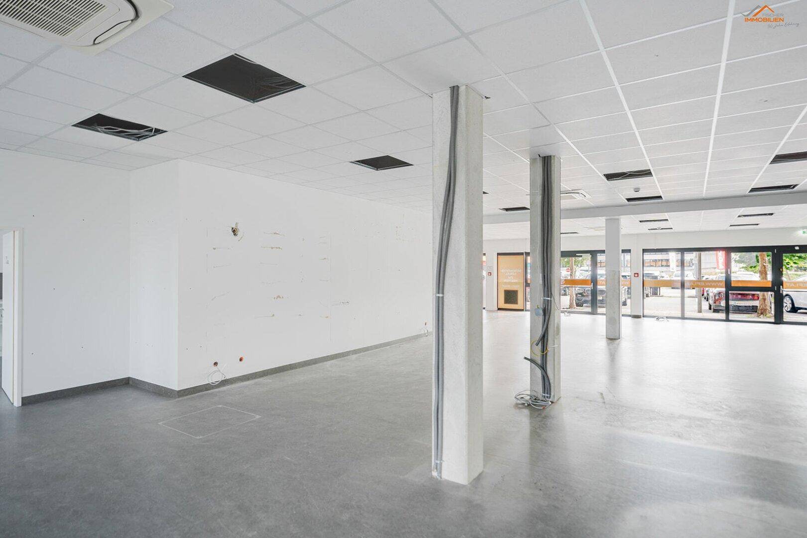 Großer, leerer Gewerberaum mit Betonboden, Säulen und sichtbaren Kabelkanälen, bereit für den Ausbau.