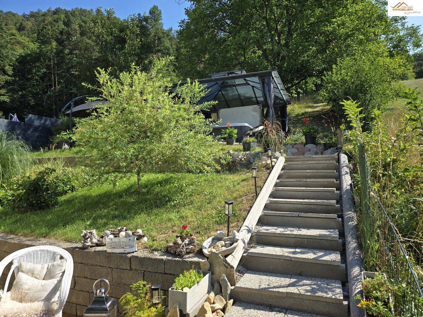 Terrassierter Gartenbereich mit Treppe, viel Grün und einem überdachten Whirlpool.