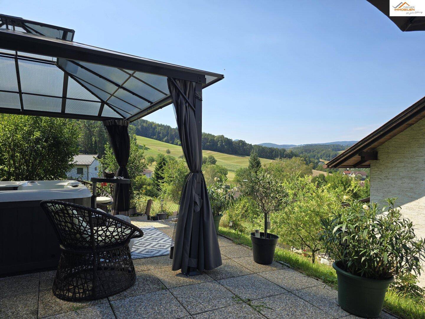 Sonniger Terrassenbereich mit überdachtem Whirlpool und weitem Blick ins Grüne.