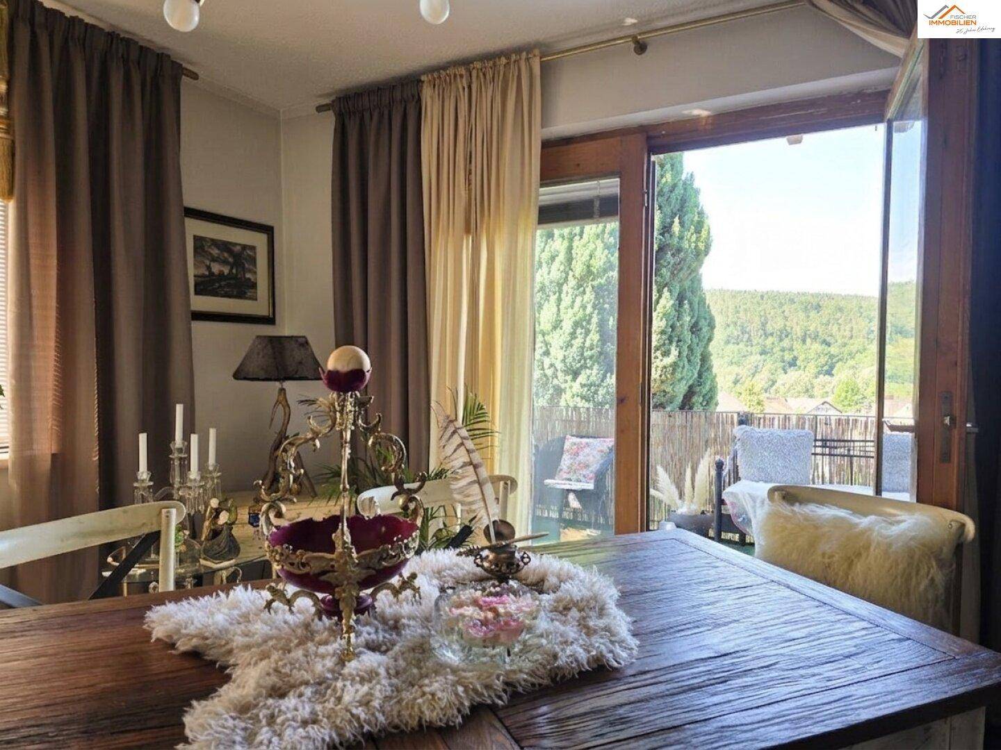 Essbereich mit Holztisch und weitem Blick ins Grüne vom angrenzenden Balkon.