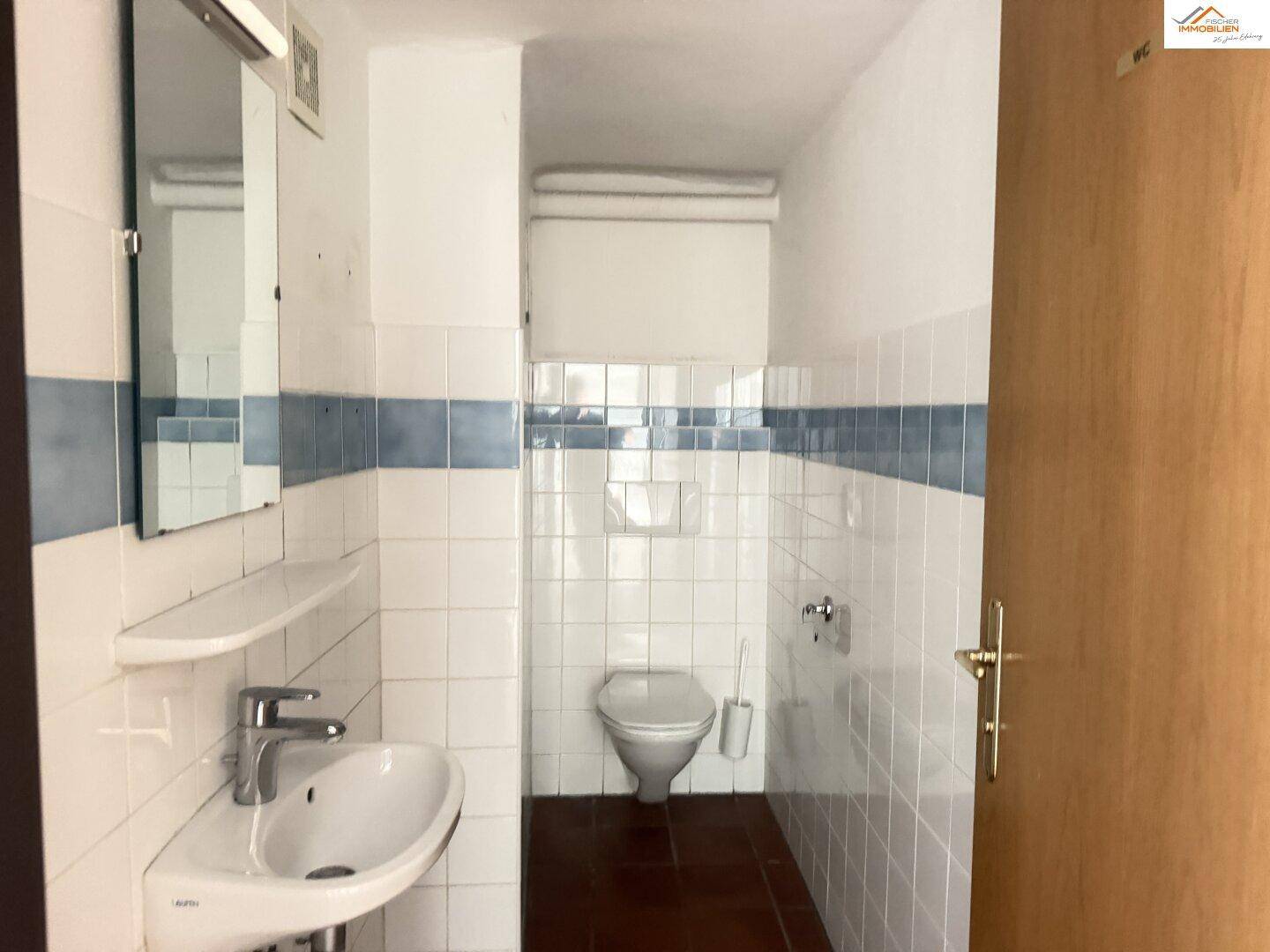 Kleines Gäste-WC mit weißen Fliesen, blauem Akzentstreifen und Wand-WC.