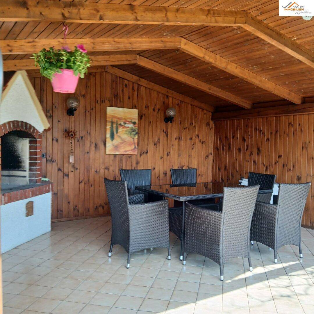 Überdachte Terrasse mit Holzwänden, Fliesenboden und gemauertem Grillbereich.