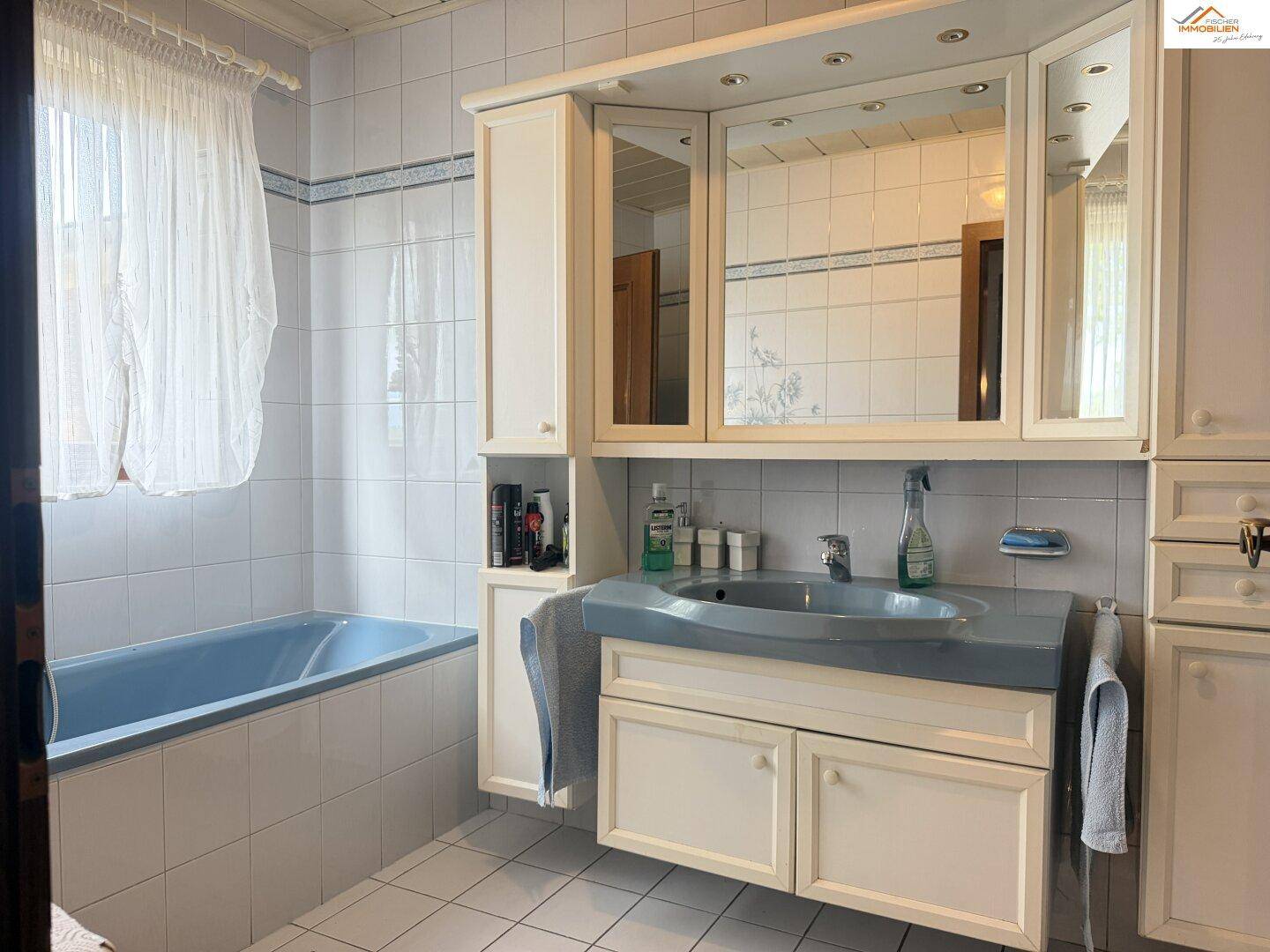 Badezimmer mit blauer Badewanne, weißen Fliesen und Spiegelschrank.