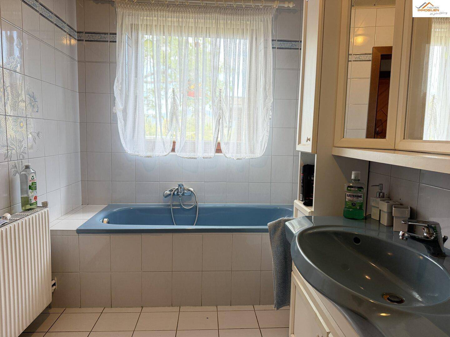 Helles Badezimmer mit Badewanne, Fenster und Heizkörper.