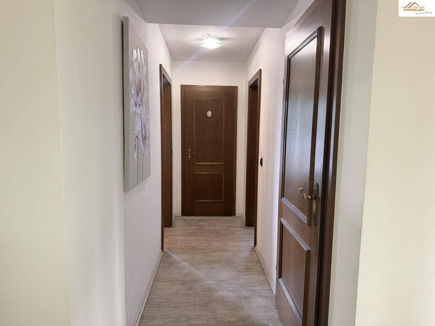 Langer Flur mit Holztüren und hellem Bodenbelag.