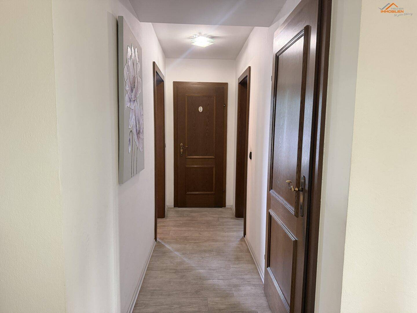 Langer Flur mit mehreren Holztüren und hellem Laminatboden, der zu weiteren Räumen führt.