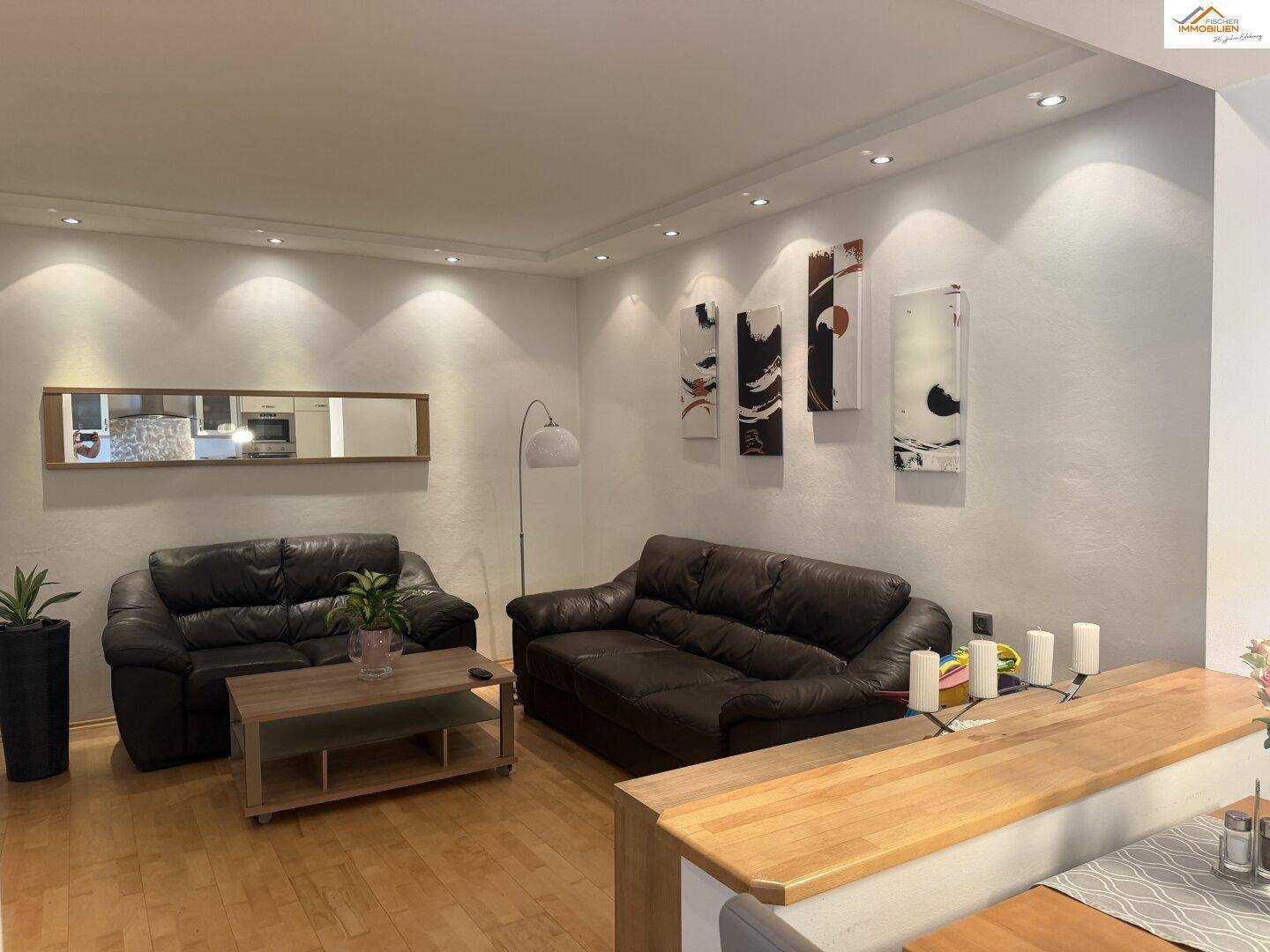 Gemütliches Wohnzimmer mit dunklen Ledersofas, Holzboden und indirekter Beleuchtung.