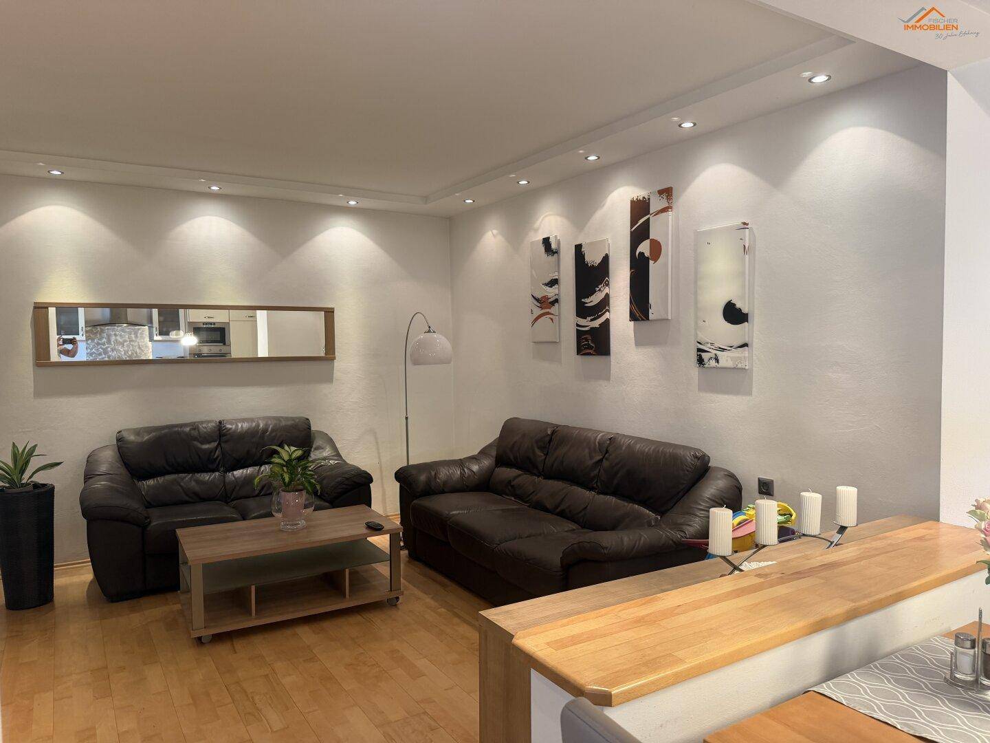 Gemütliches Wohnzimmer mit dunklen Ledersofas, Couchtisch und moderner Wanddekoration.