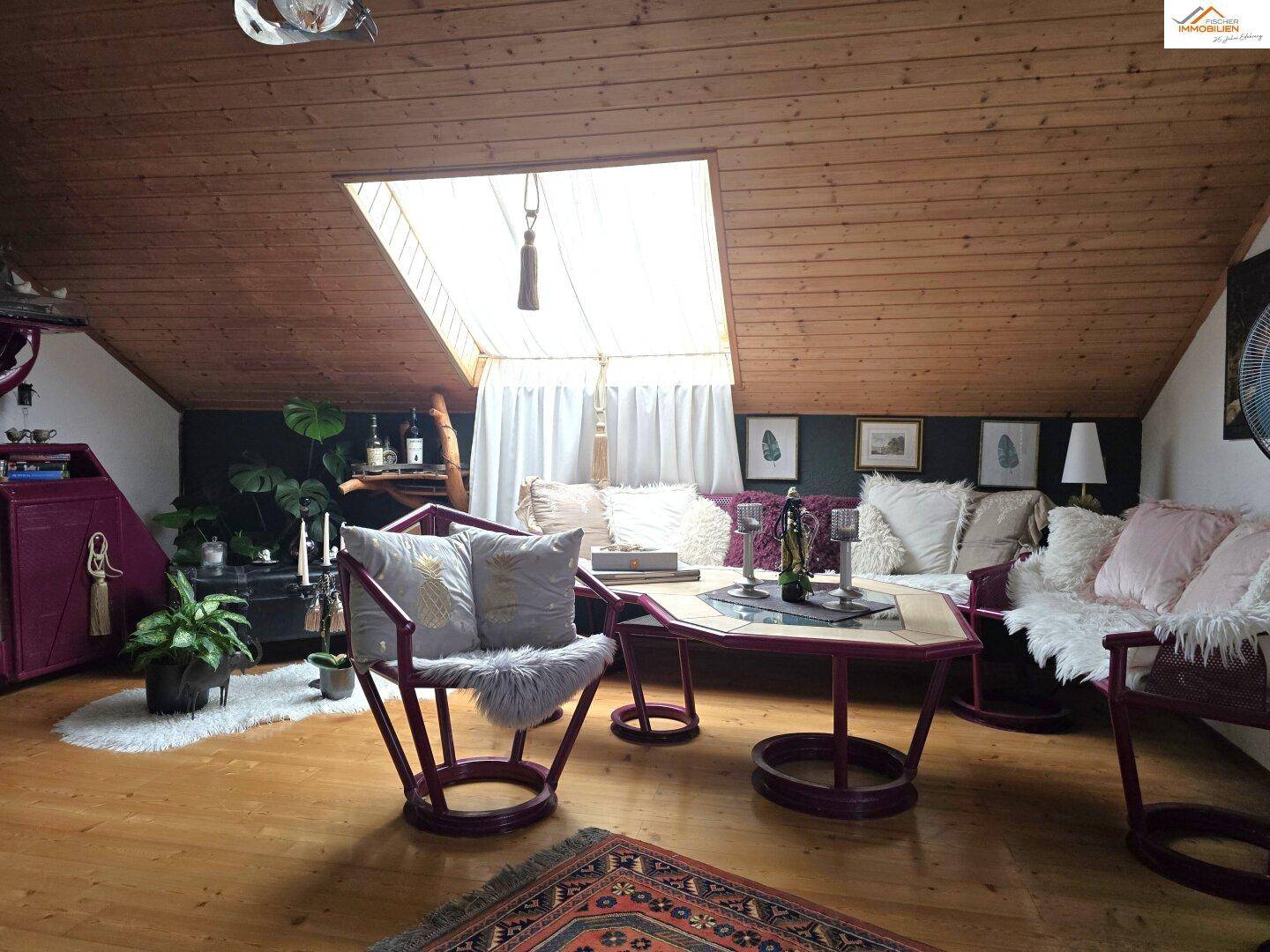 Helles Wohnzimmer im Dachgeschoss mit Holzdecke, Dachfenster und farbenfroher Einrichtung.