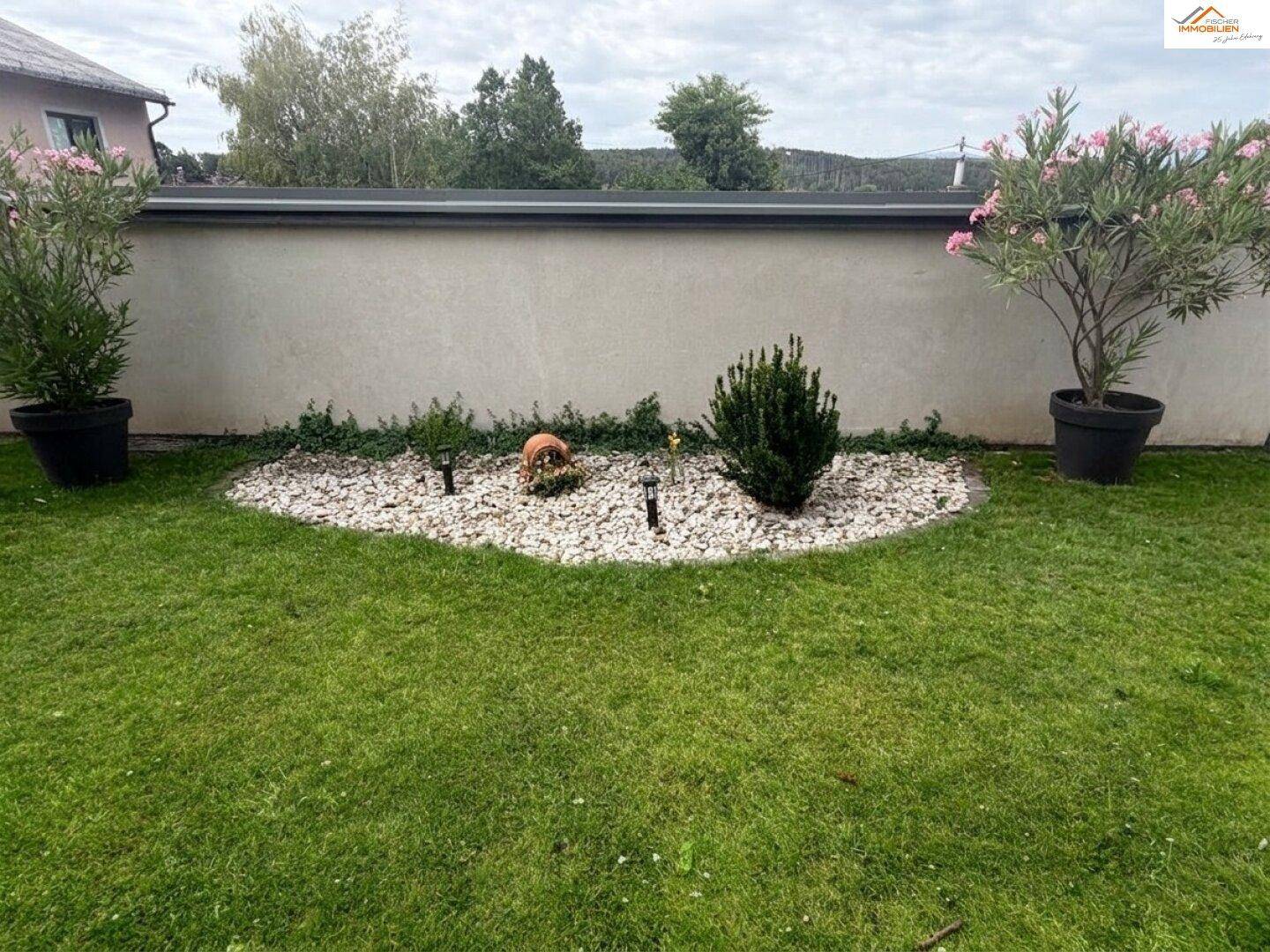Gepflegter Gartenbereich mit Ziersteinen, Rasenfläche und blühenden Pflanzen.