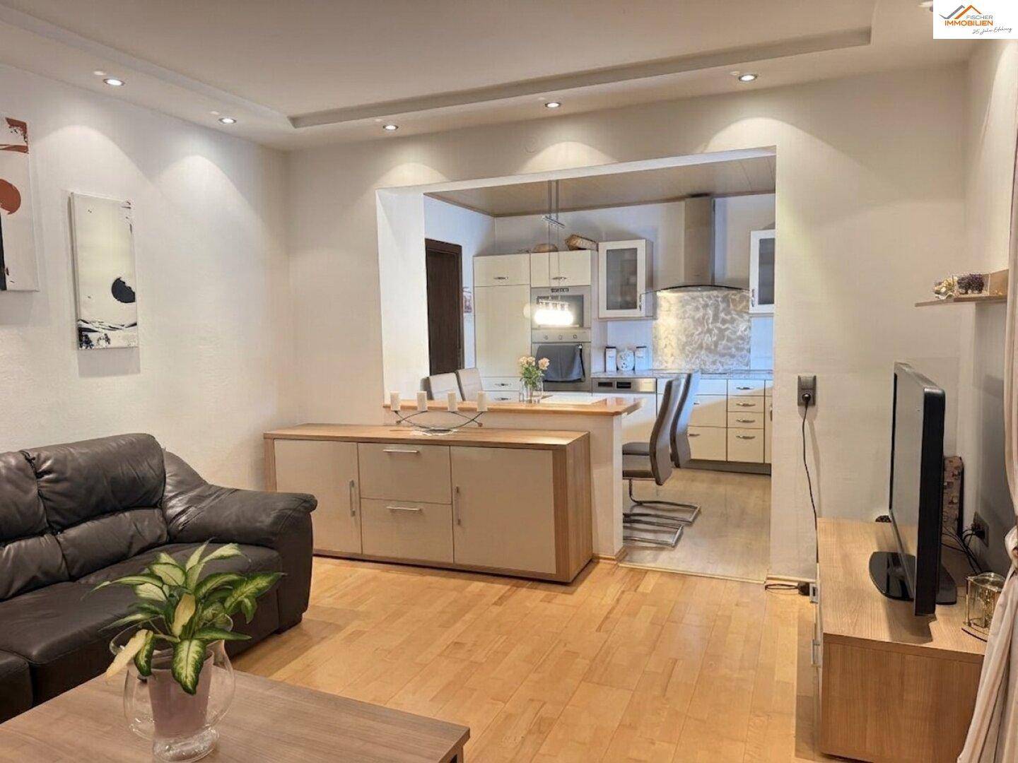 Offener Wohnbereich mit Sofa, Fernseher und Blick in die angrenzende Küche.