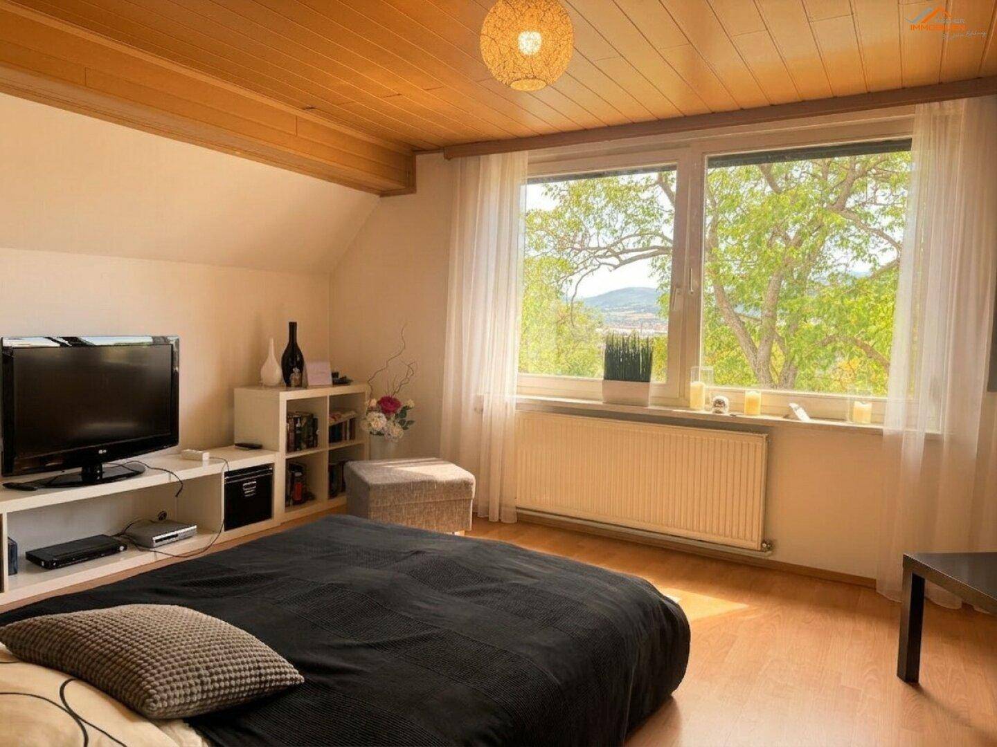 Schlafzimmer mit Doppelbett, Fernseher und großem Fenster mit Blick ins Grüne.