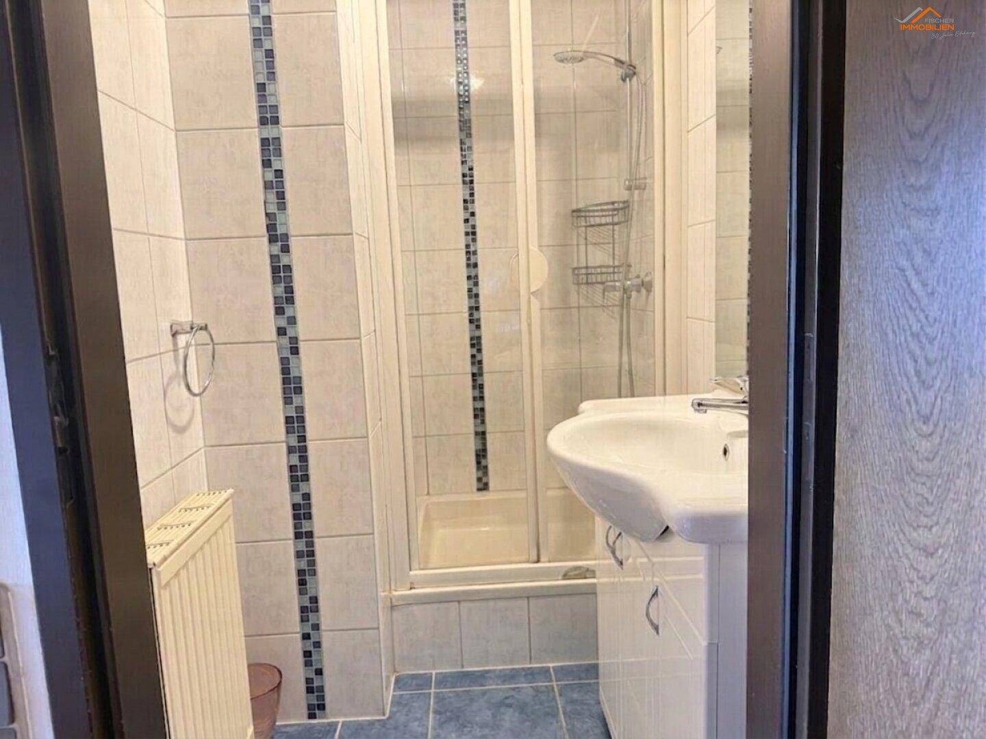 Kleines Badezimmer mit Duschkabine, Waschbecken und blauen Bodenfliesen, funktional eingerichtet.