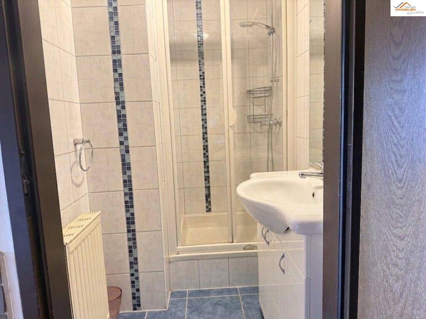 Kleines Badezimmer mit Duschkabine, Waschtisch und blauen Akzentfliesen.