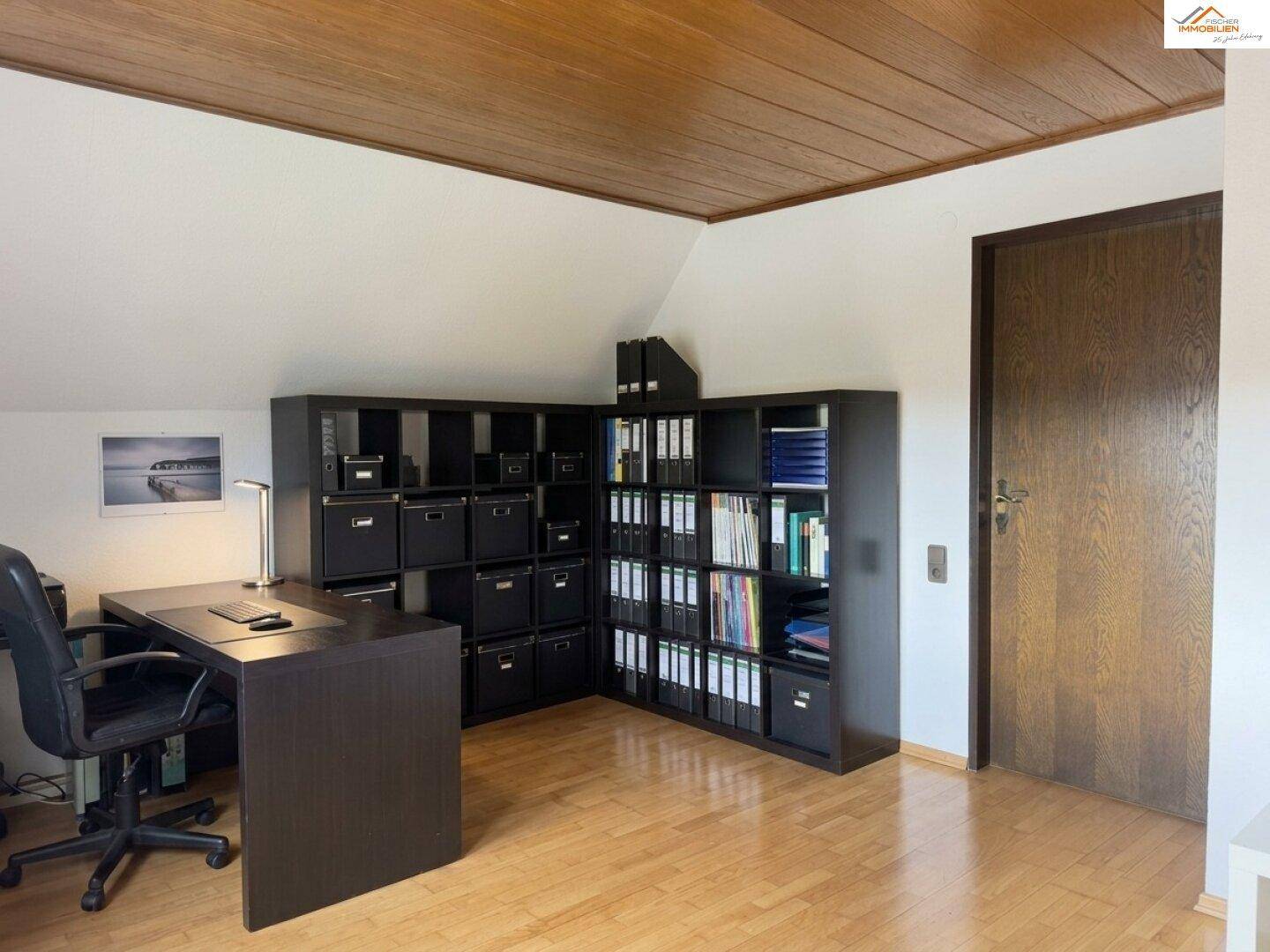 Helles Arbeitszimmer mit großem Schreibtisch, Regalen und Holzbalkendecke.