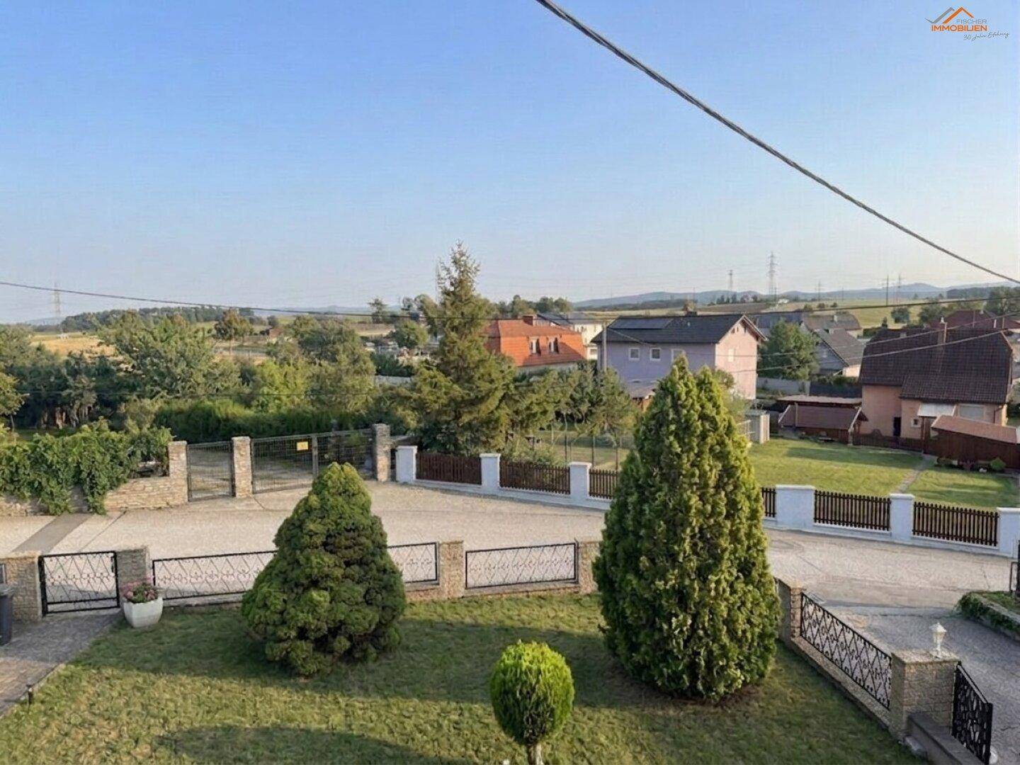 Weitläufiger Blick über die ländliche Umgebung mit weiteren Häusern und Feldern unter blauem Himmel.