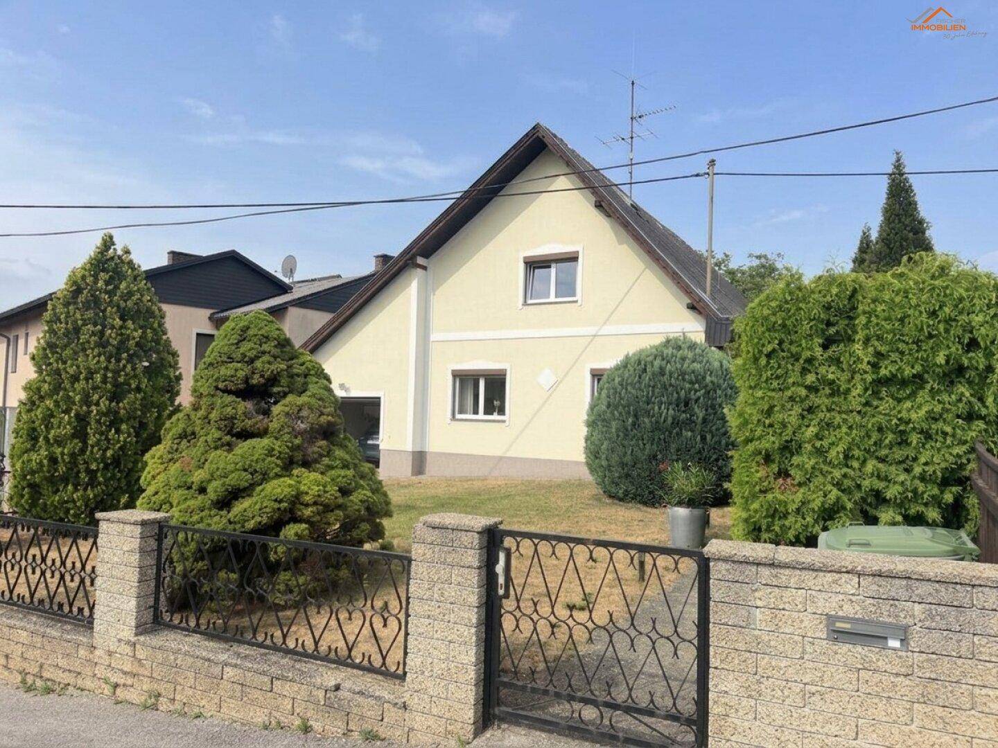 Ansicht des Einfamilienhauses von der Straße mit Vorgarten und schmiedeeisernem Zaun.