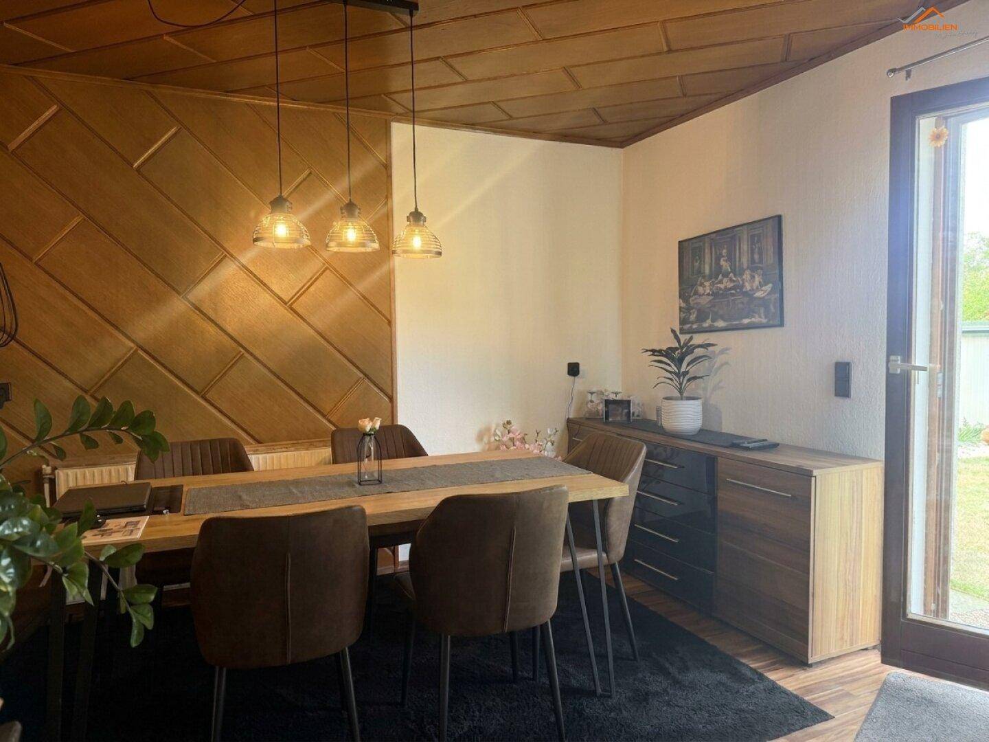 Gemütlicher Essbereich mit Holztisch, modernen Stühlen und dekorativer Holzvertäfelung an der Wand.