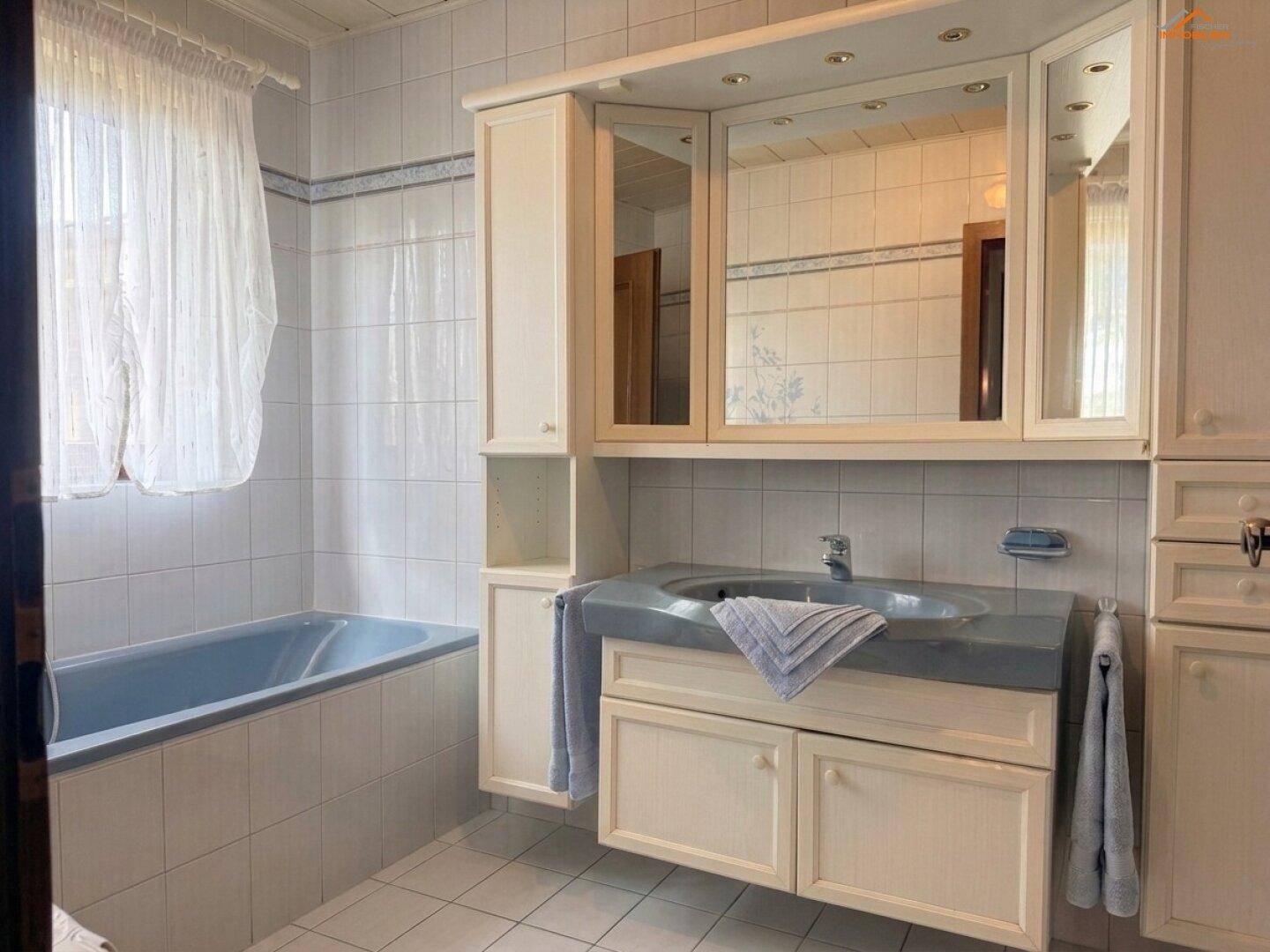 Badezimmer mit blauer Badewanne, Waschbecken und hellen Fliesen an Wänden und Boden.