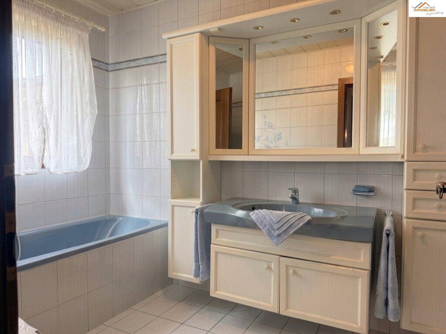 Badezimmer mit blauer Badewanne, Waschtisch und Spiegelschrank in hellem Design.