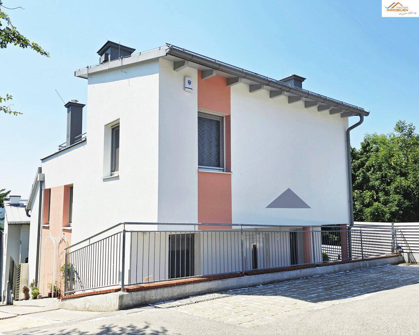 Seitenansicht des Hauses mit weißer und pfirsichfarbener Fassade und Zufahrtsrampe.