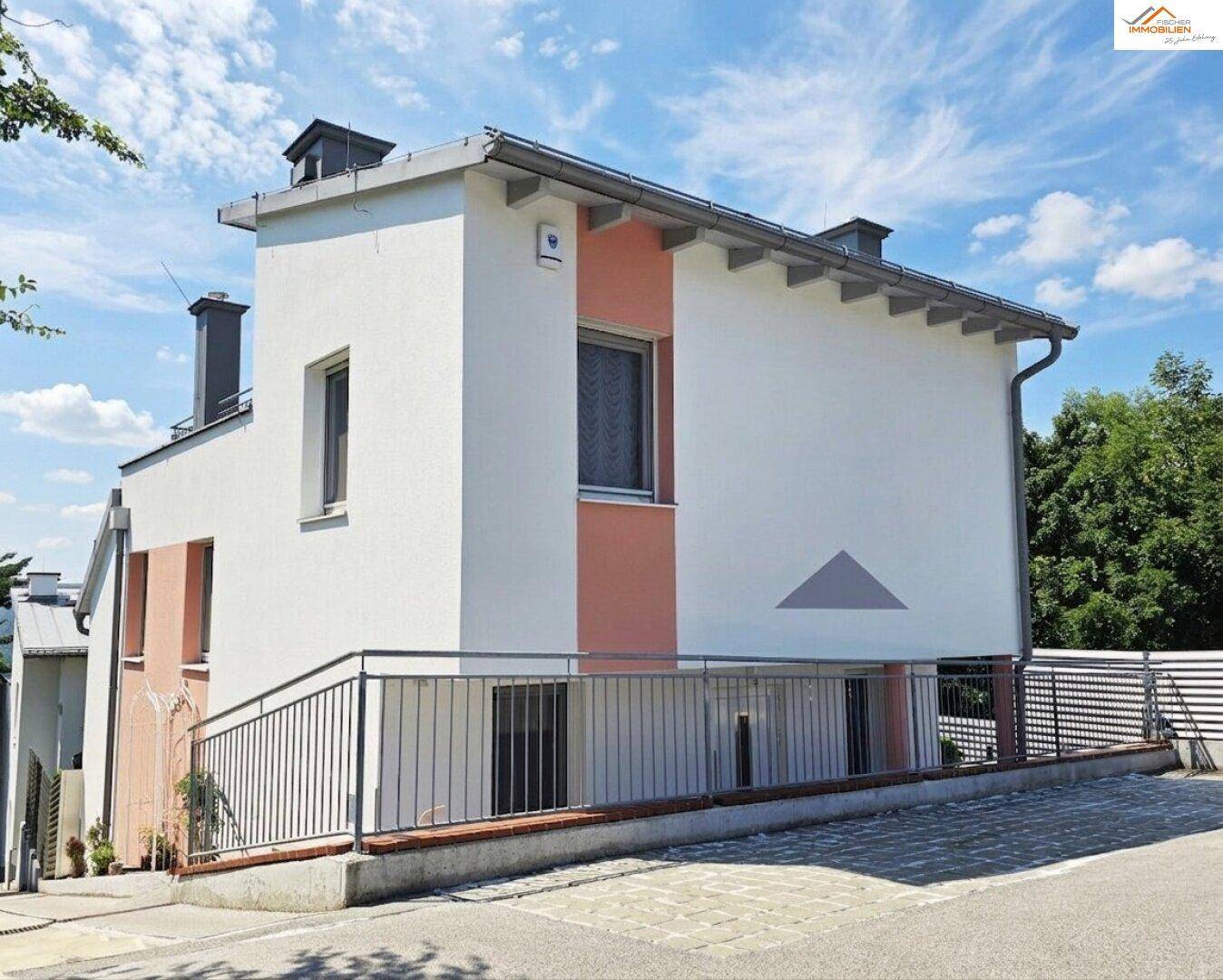 Seitenansicht des Hauses mit weißer und pfirsichfarbener Fassade und Zufahrtsrampe.